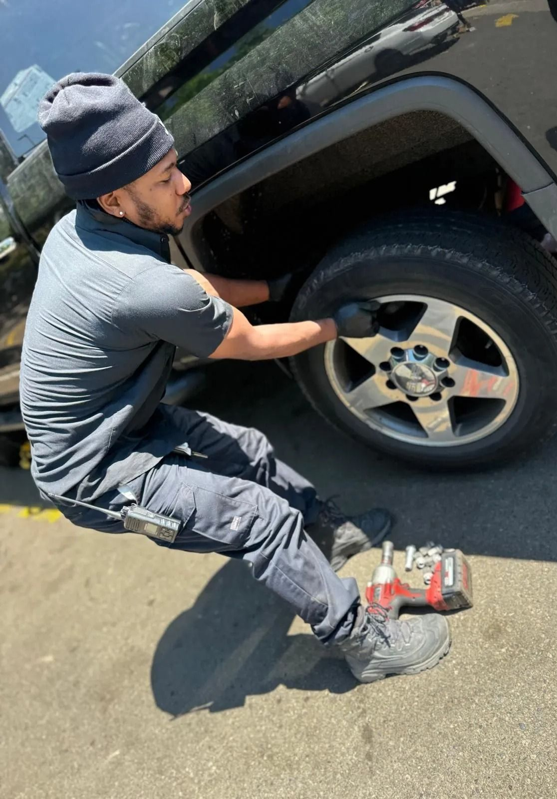 A person in dark clothing changes a tire on a black vehicle, with tools nearby.