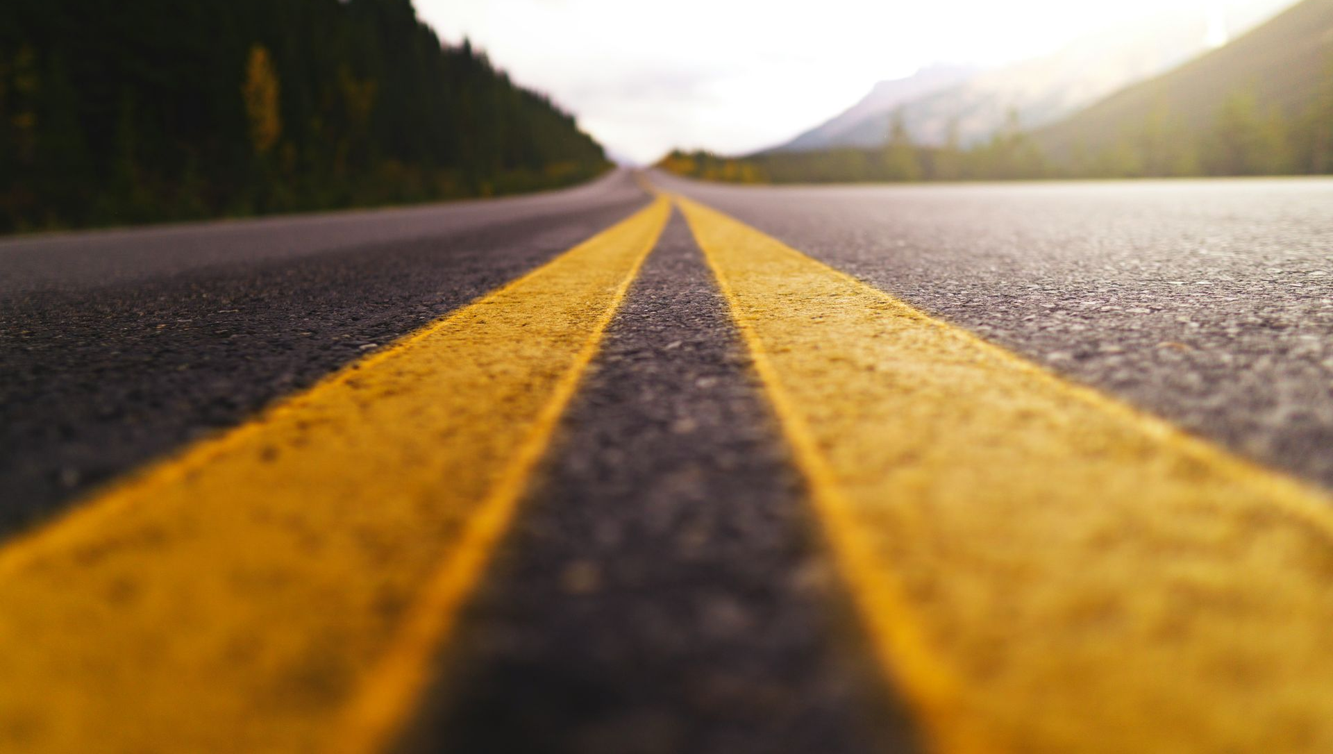 Low-angle view of a yellow-striped road stretching into a misty mountain landscape at sunrise