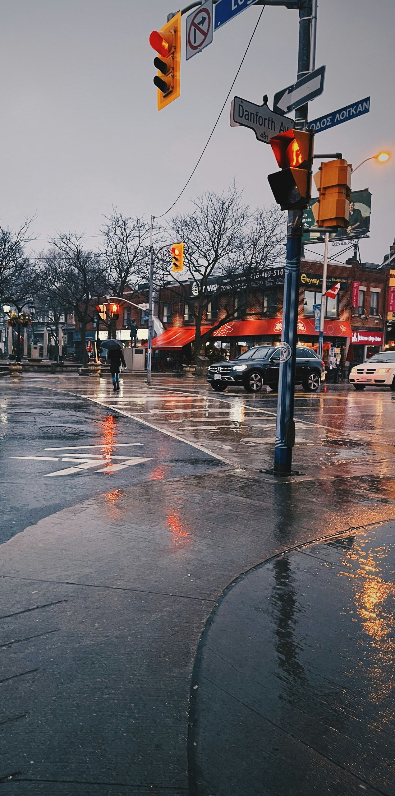Rainy city street with wet pavement, traffic lights, and storefronts reflecting orange lights.