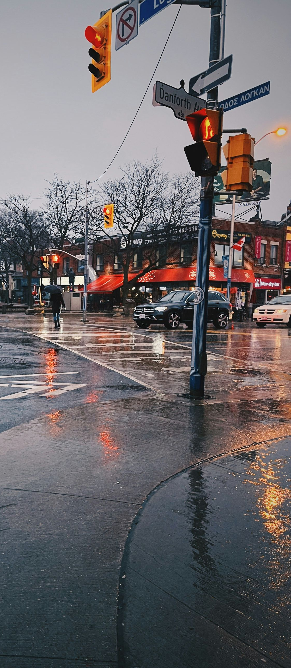 Rainy city street with wet pavement, traffic lights, and storefronts reflecting orange lights.