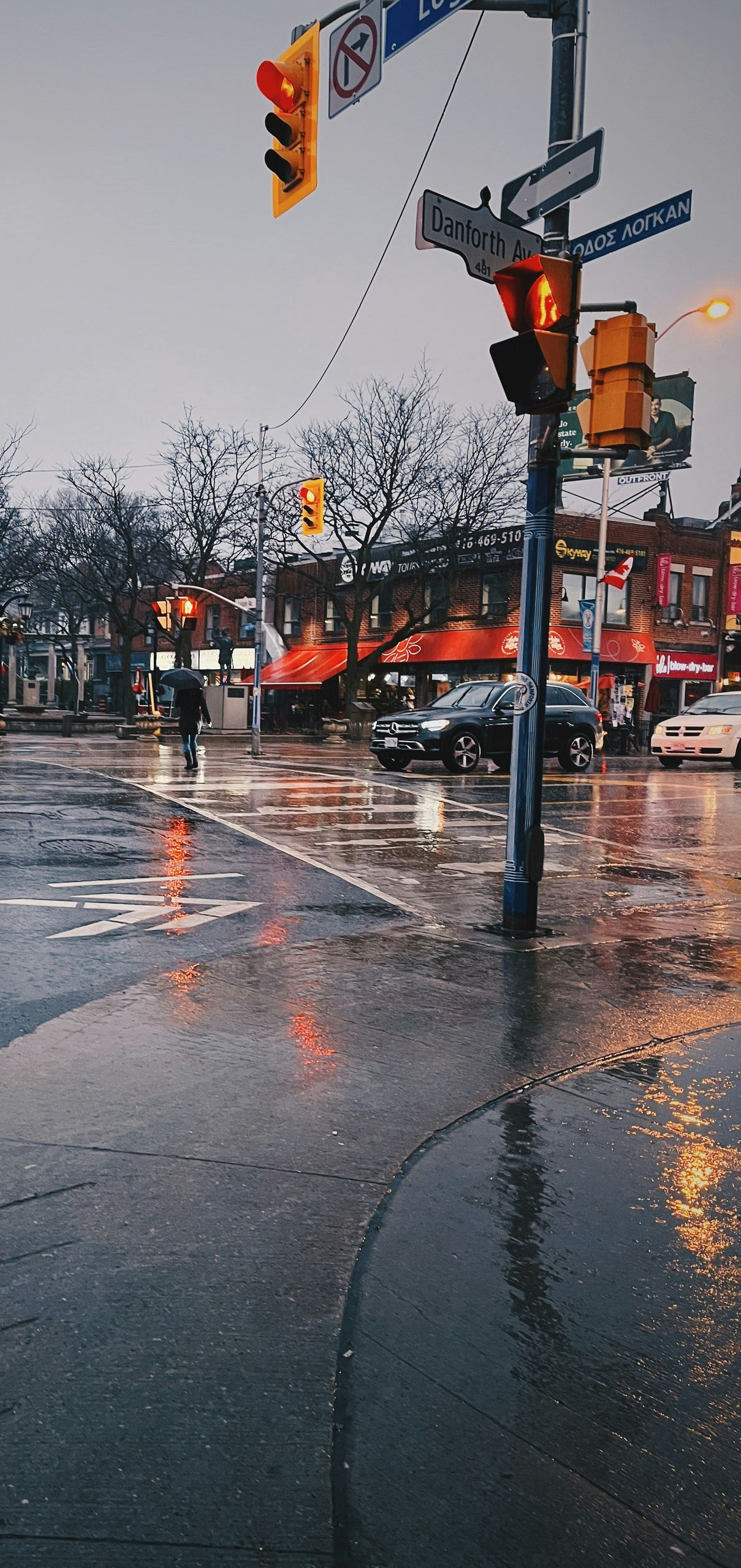 Rainy city street with wet pavement, traffic lights, and storefronts reflecting orange lights.