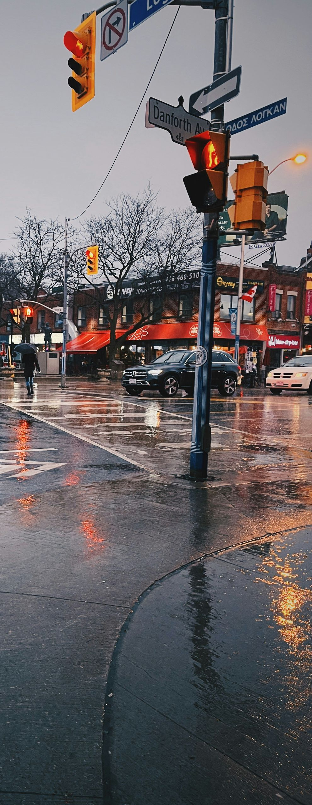 Rainy city street with wet pavement, traffic lights, and storefronts reflecting orange lights.