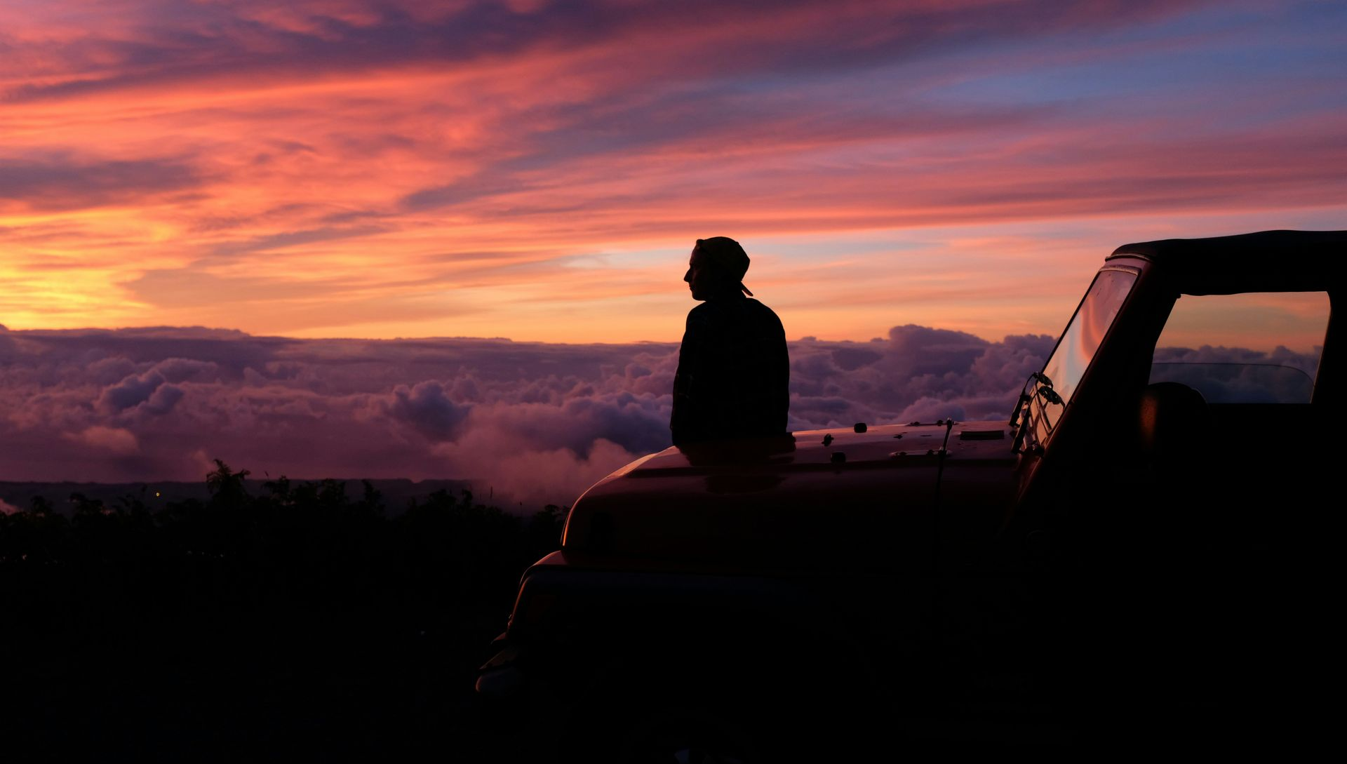 Silhouette of a person sitting on a vehicle at sunset under a pink-orange sky.