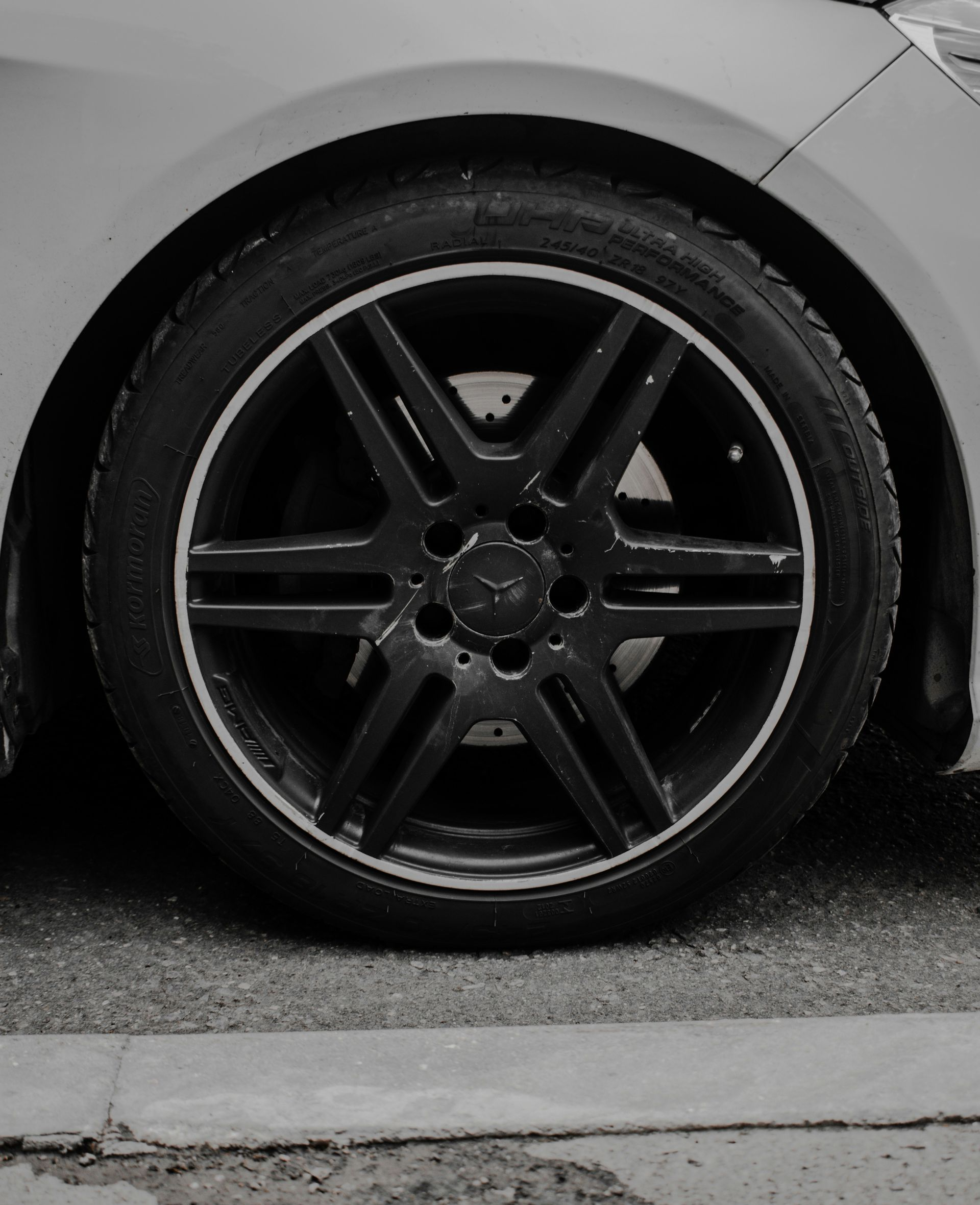 Close-up of a car’s black alloy wheel and tire on wet pavement, with gray body panel above