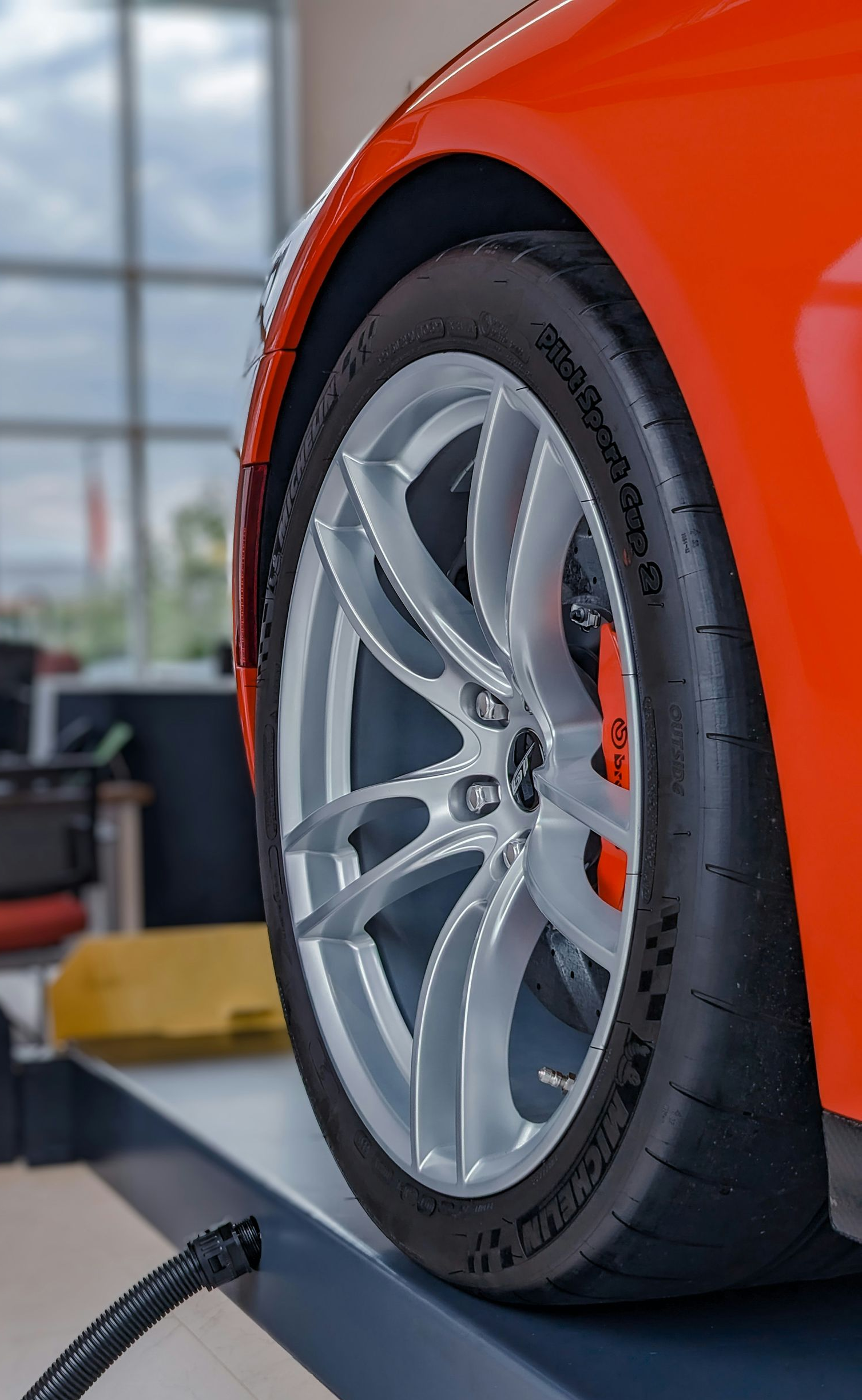 A close-up view of an orange car wheel with a silver rim on a lift inside an auto repair shop.