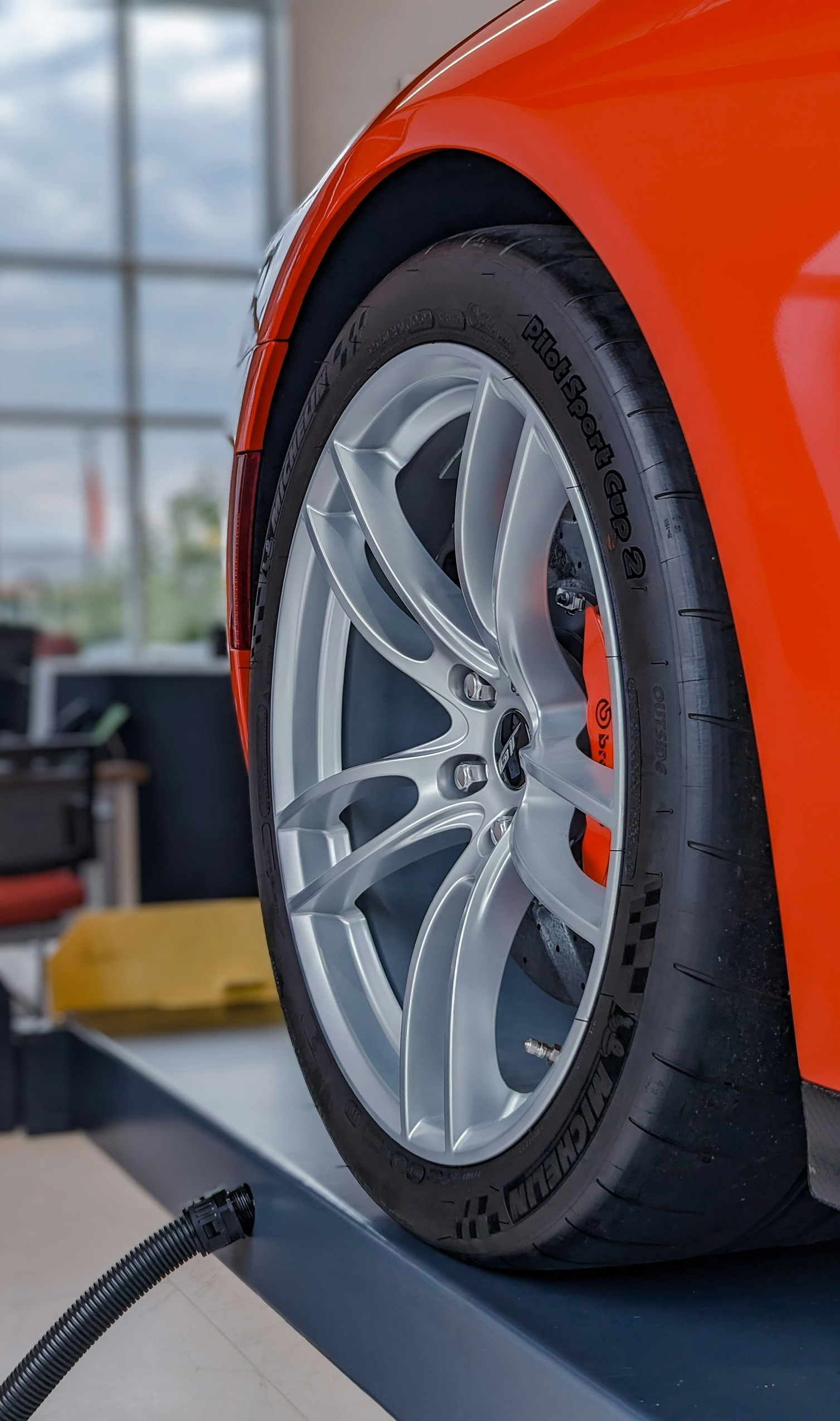 A close-up view of an orange car wheel with a silver rim on a lift inside an auto repair shop.