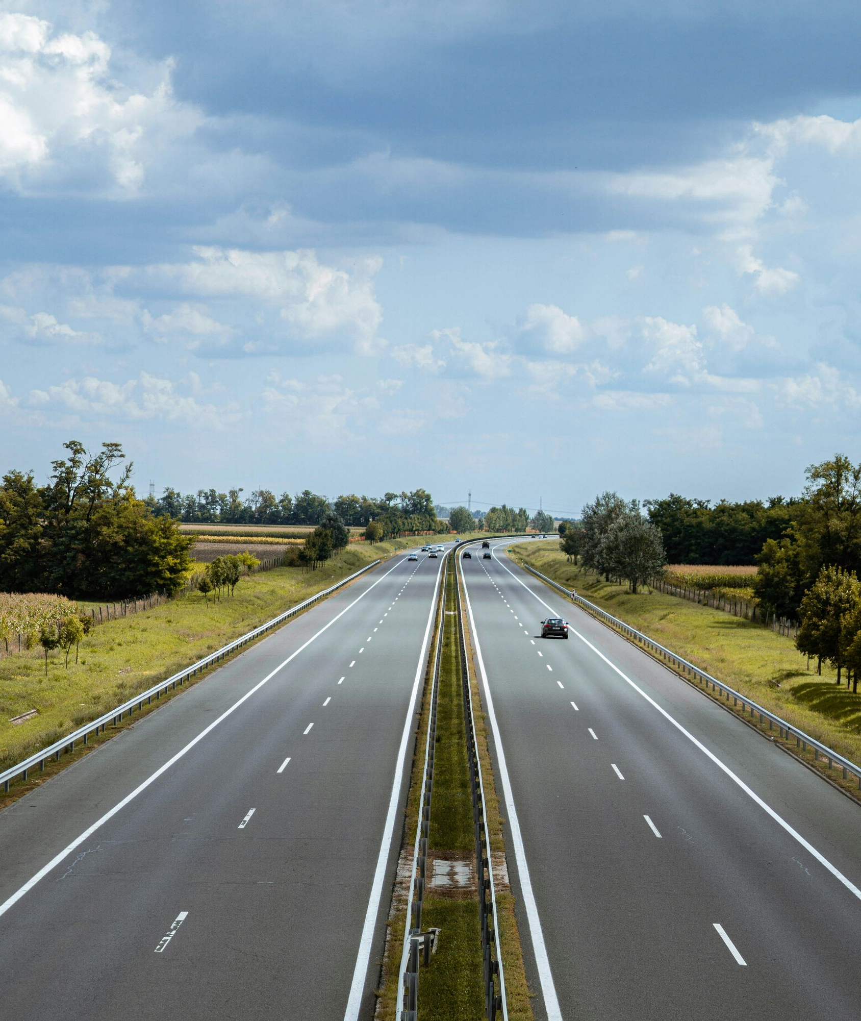 Highway stretches between green fields under a cloudy sky.
