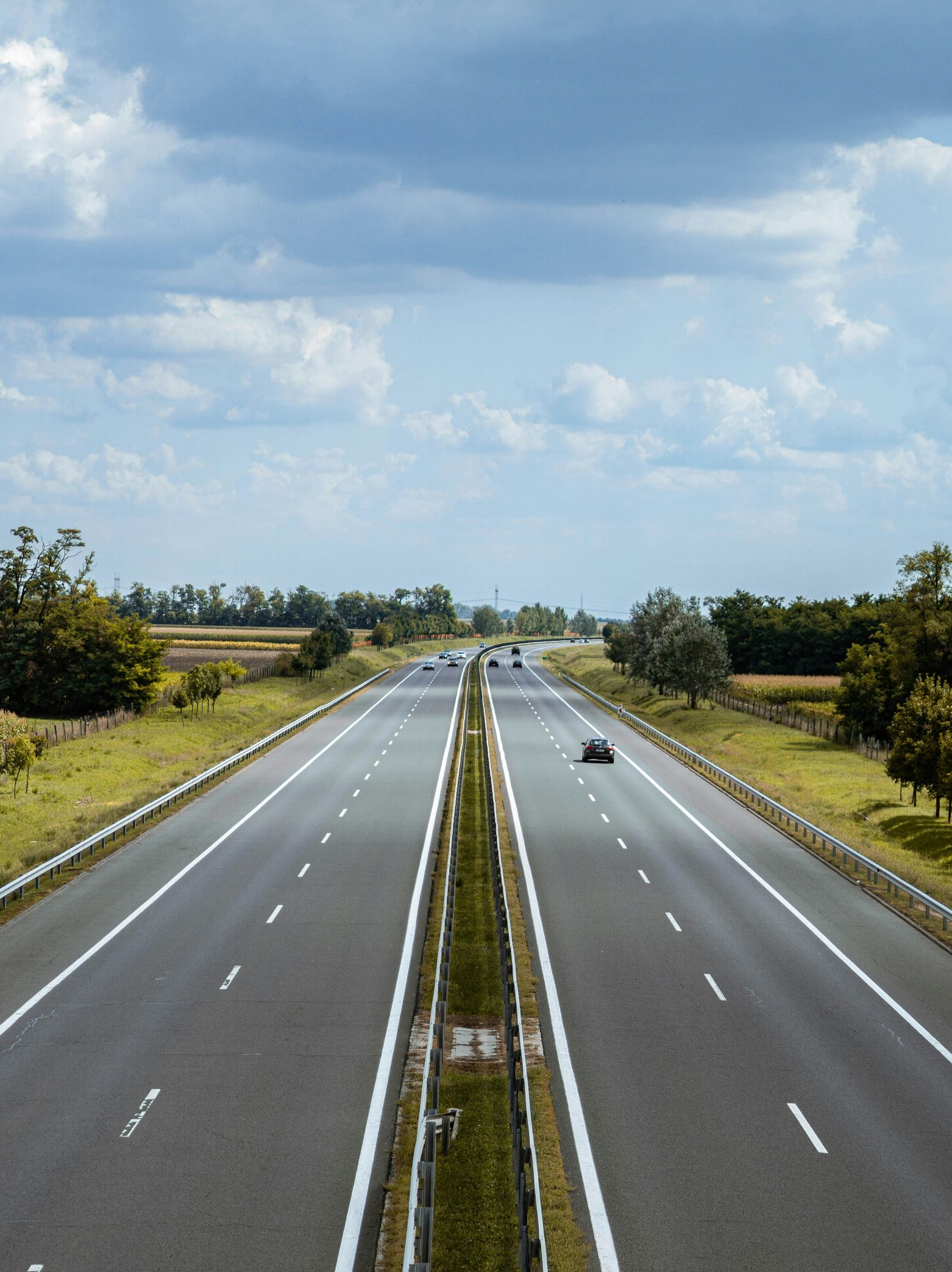 Highway stretches between green fields under a cloudy sky.