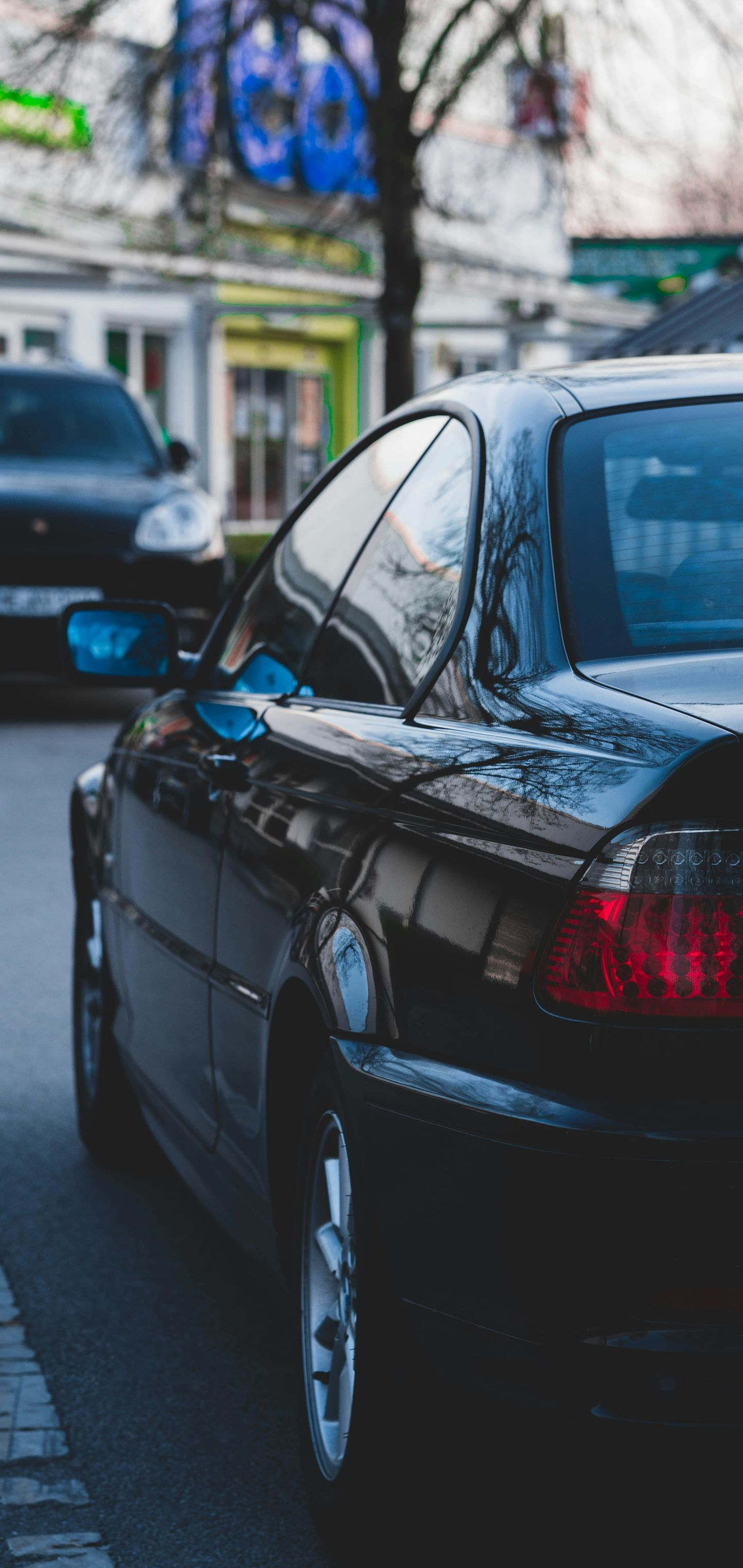 Black car parked on a street; another car visible in the background.