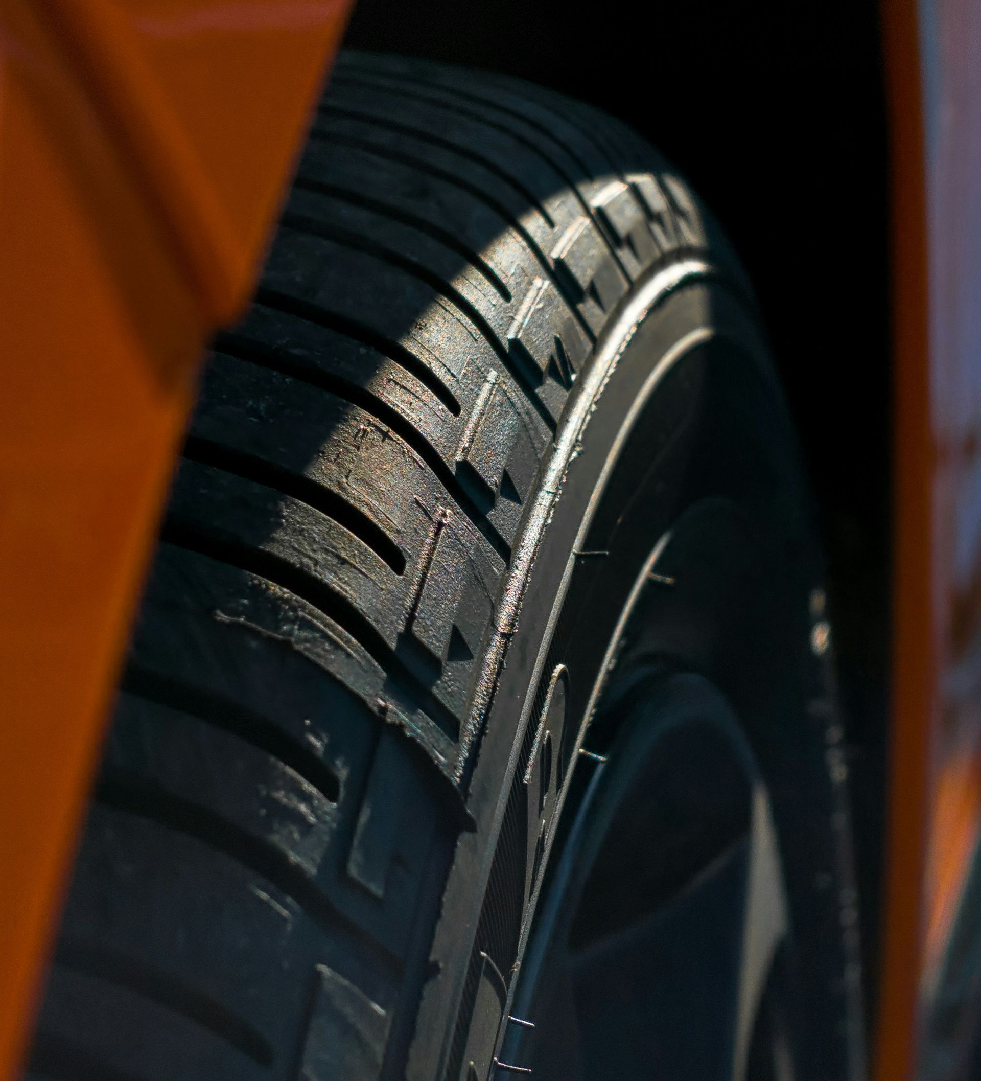 Close-up of a car tire tread beside an orange vehicle body