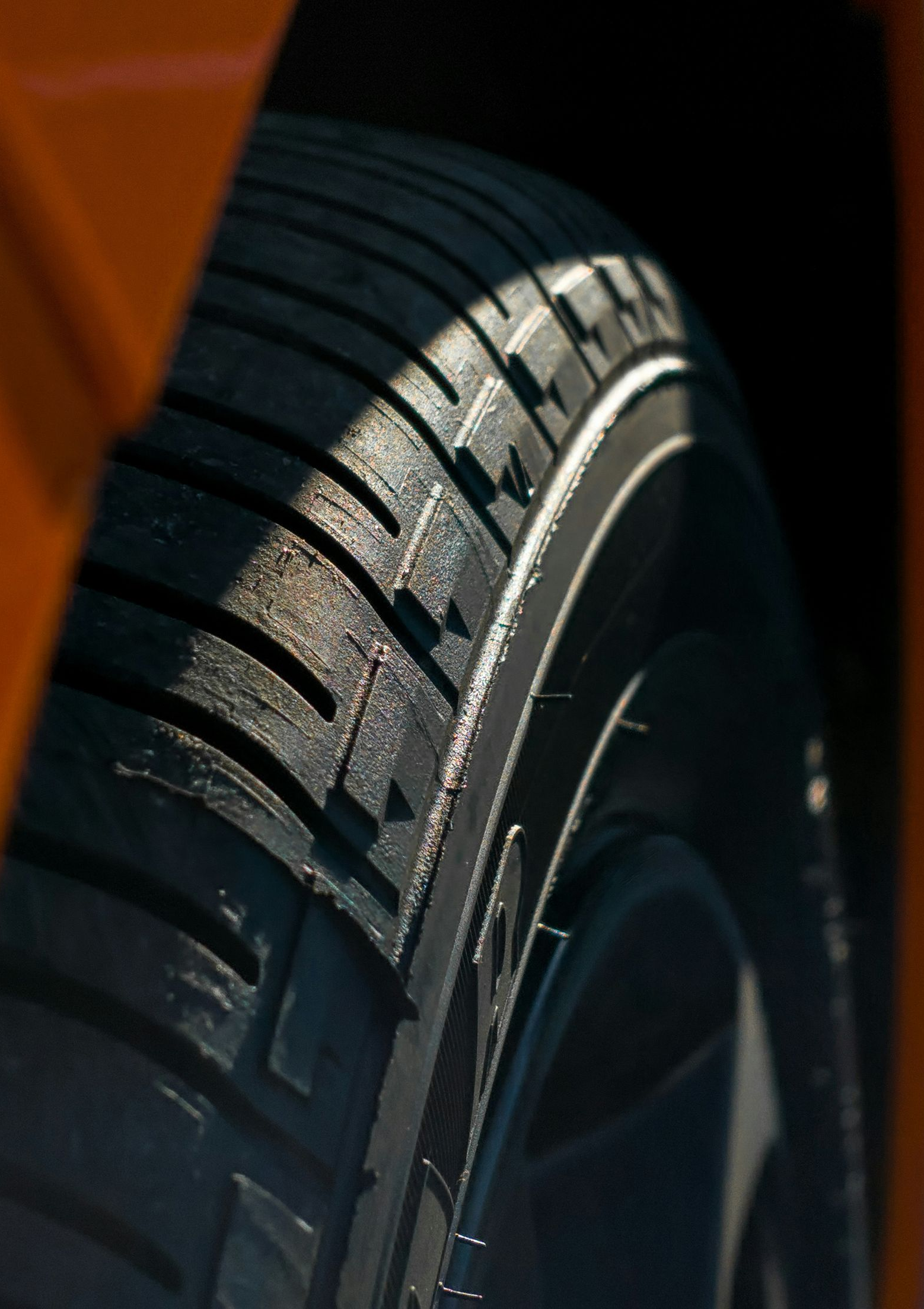 Close-up of a car tire tread beside an orange vehicle body