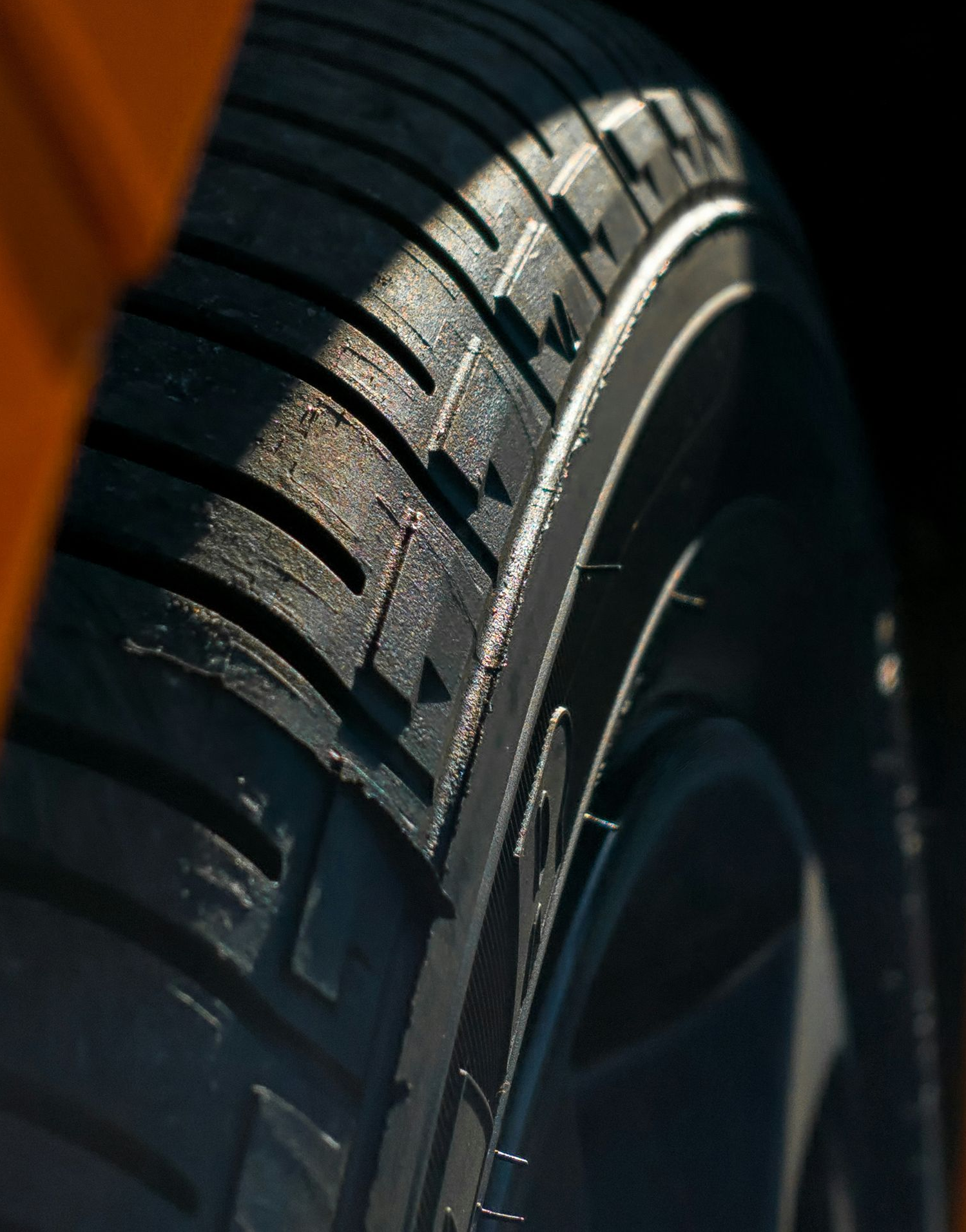Close-up of a car tire tread with dark rubber and sunlight highlighting the sidewall