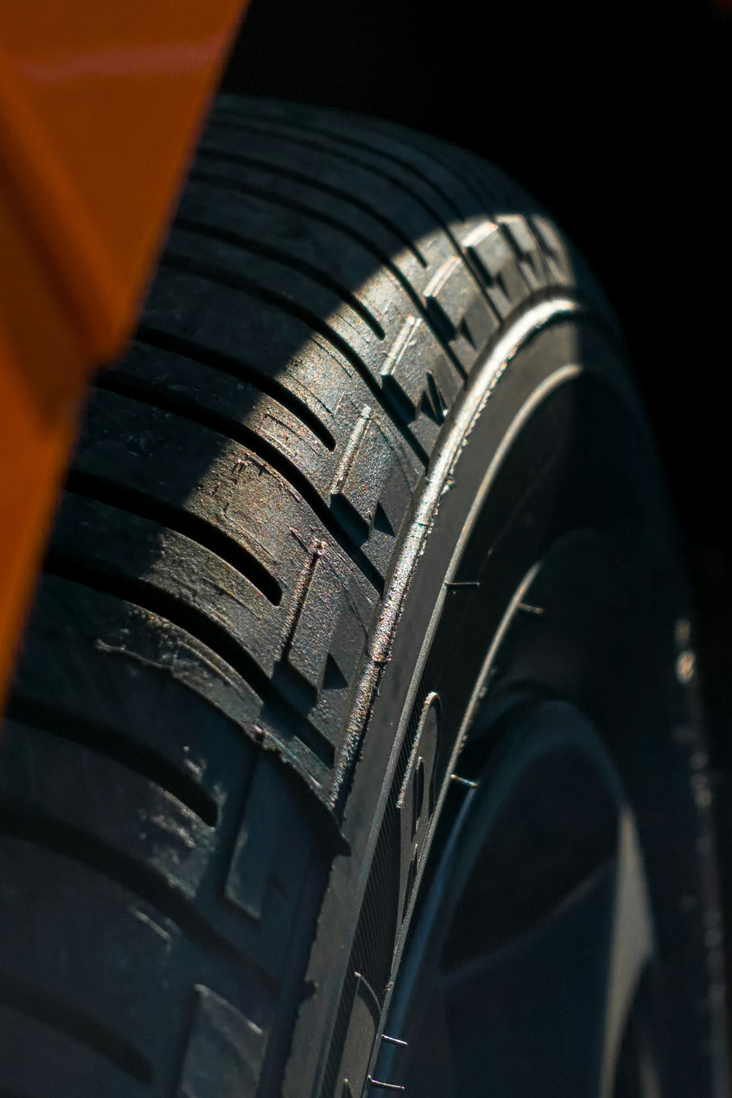 Close-up of a car tire tread beside an orange vehicle body