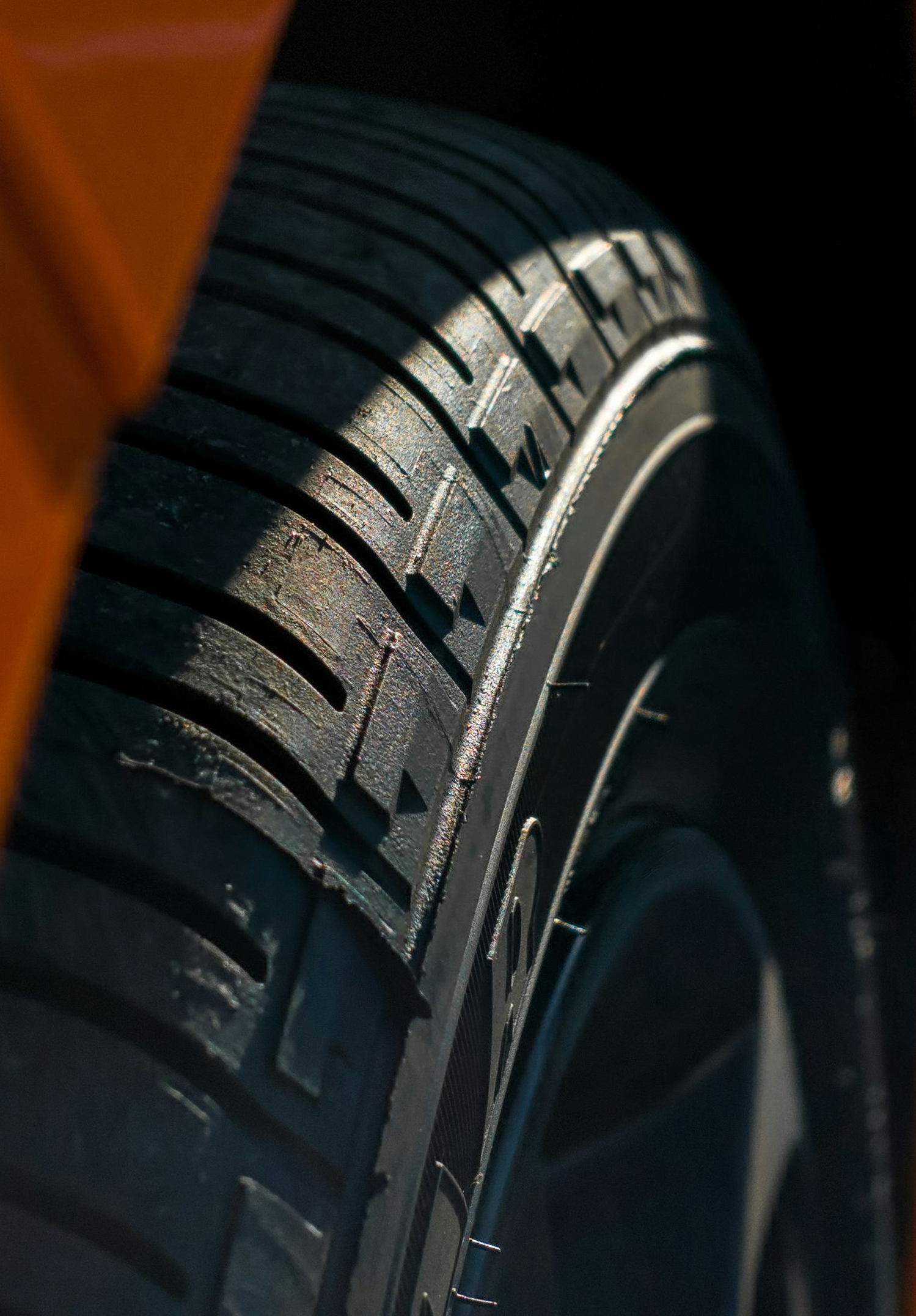 Close-up of a car tire tread with dark rubber and sunlight highlighting the sidewall