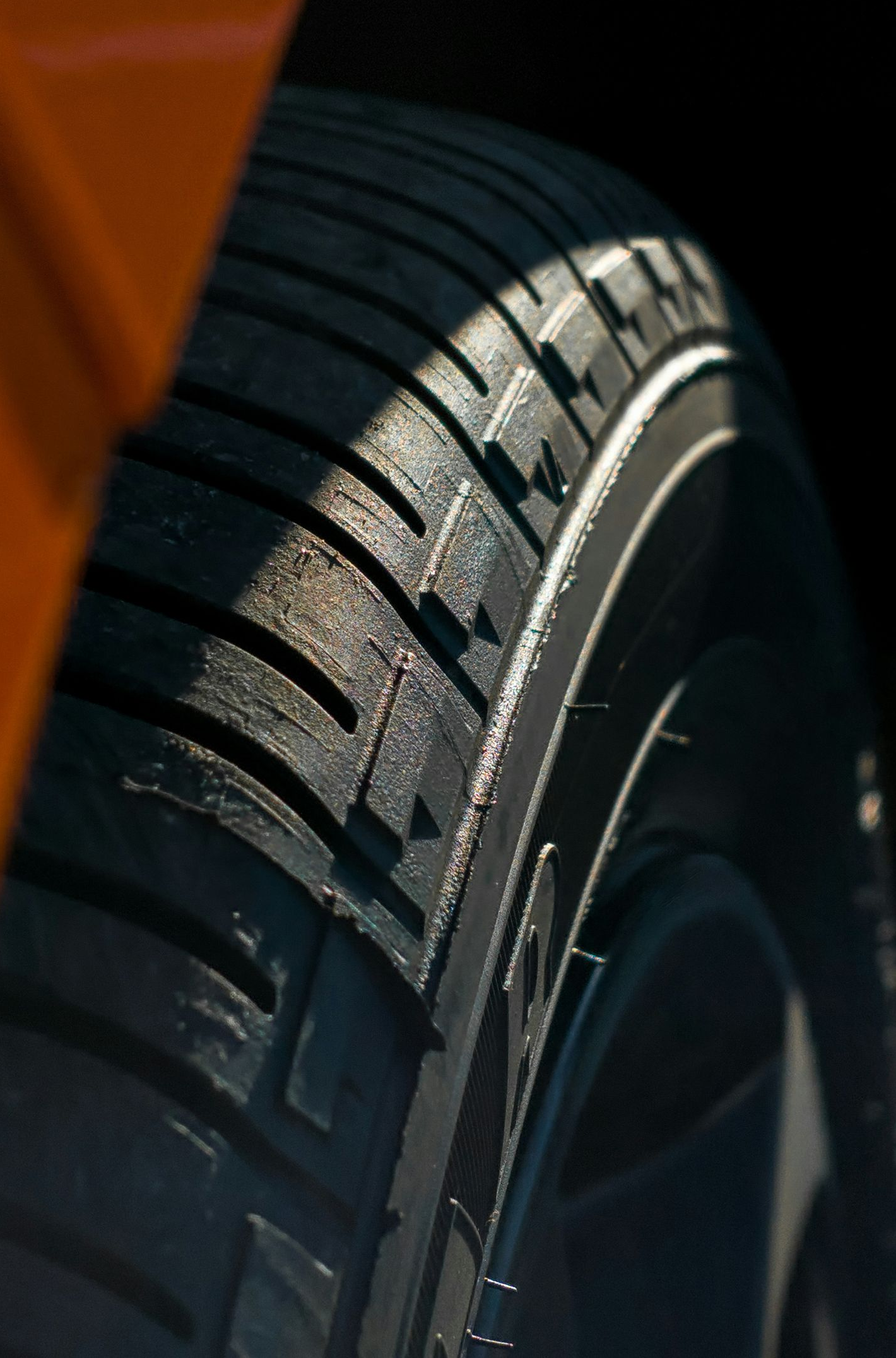 Close-up of a car tire tread with dark rubber and sunlight highlighting the sidewall
