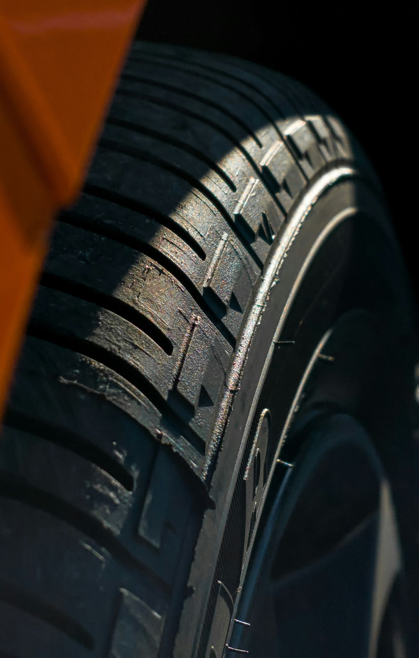 Close-up of a car tire tread with dark rubber and sunlight highlighting the sidewall