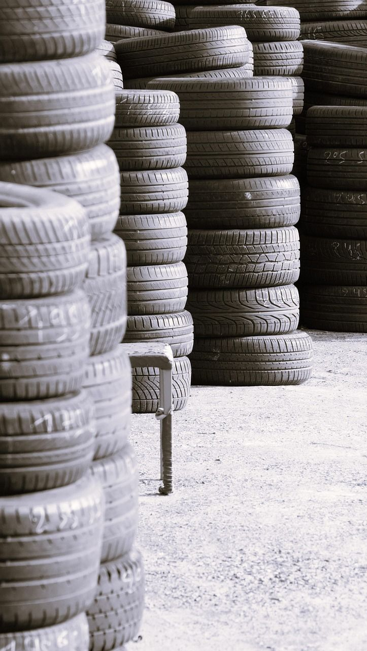 Stacks of tires in a storage area, rows of black tires, a metal stool on the ground.
