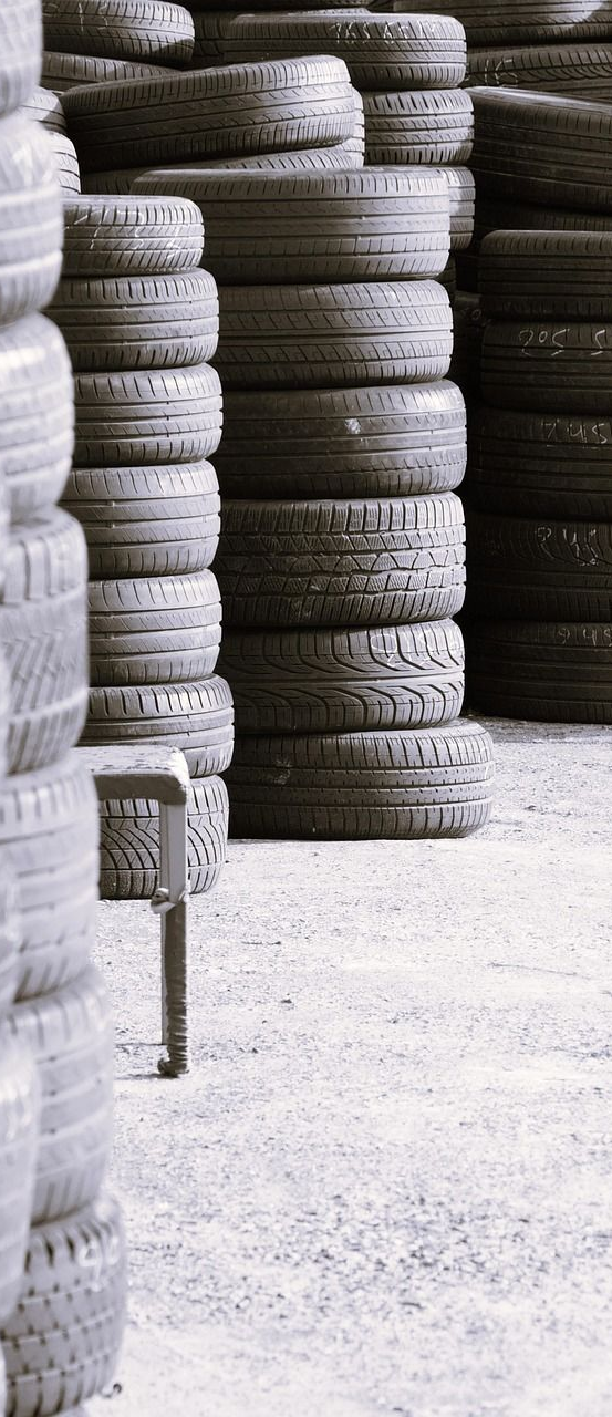 Stacks of tires in a storage area, rows of black tires, a metal stool on the ground.