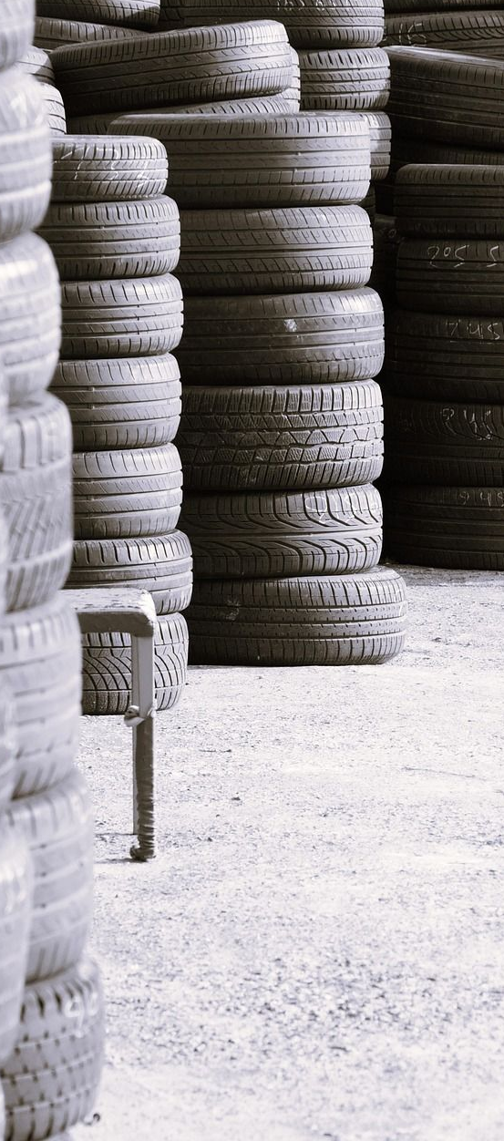 Stacks of tires in a storage area, rows of black tires, a metal stool on the ground.