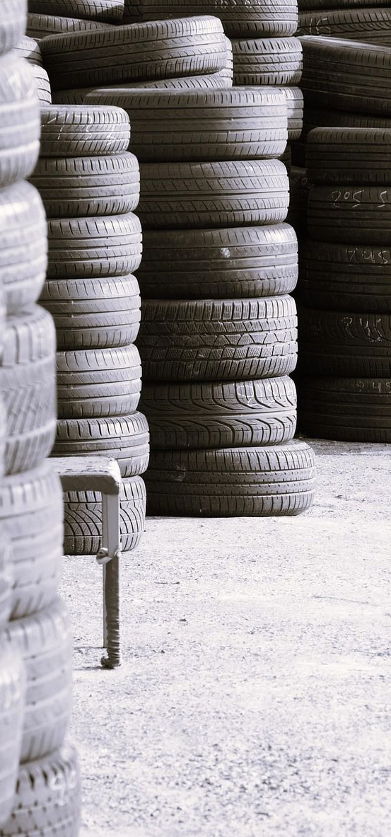 Stacks of used tires in an outdoor setting, arranged vertically, gray tones.