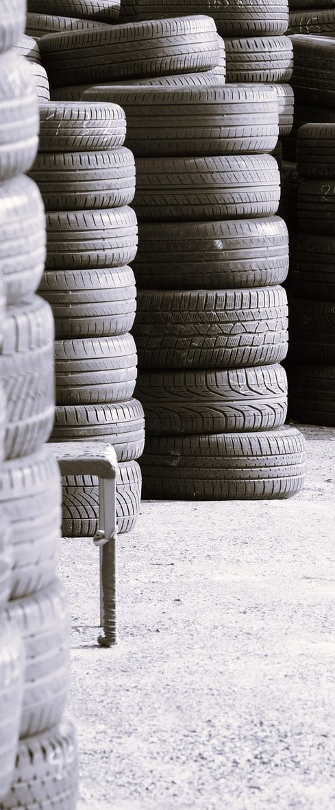 Stacks of used tires in an outdoor setting, arranged vertically, gray tones.