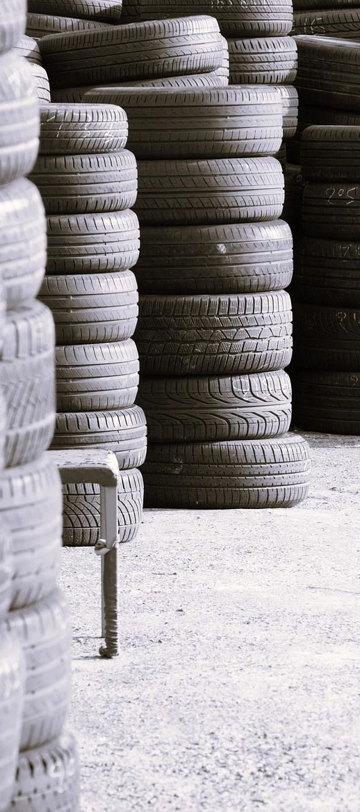 Stacks of used tires in an outdoor setting, arranged vertically, gray tones.