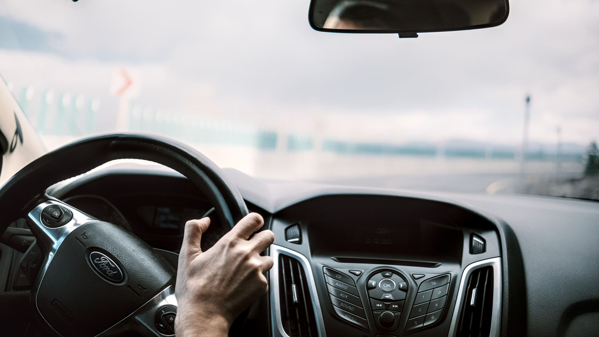 Driver’s hands on the steering wheel inside a car, with a road visible through the windshield.