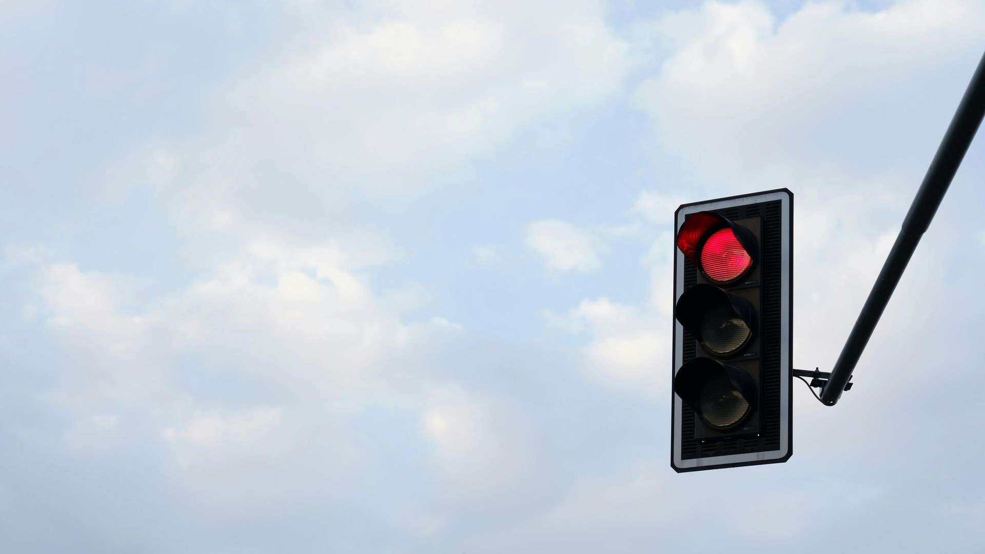 Red traffic light against a cloudy sky, mounted on a street pole.
