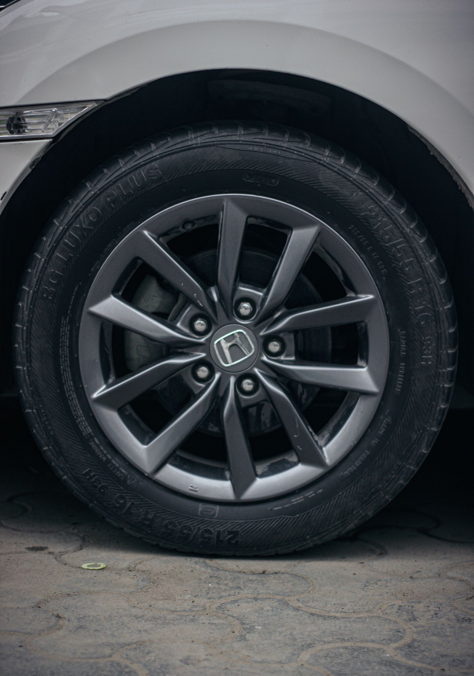 Close-up of a car’s front wheel with a black tire and gray alloy rim on pavement