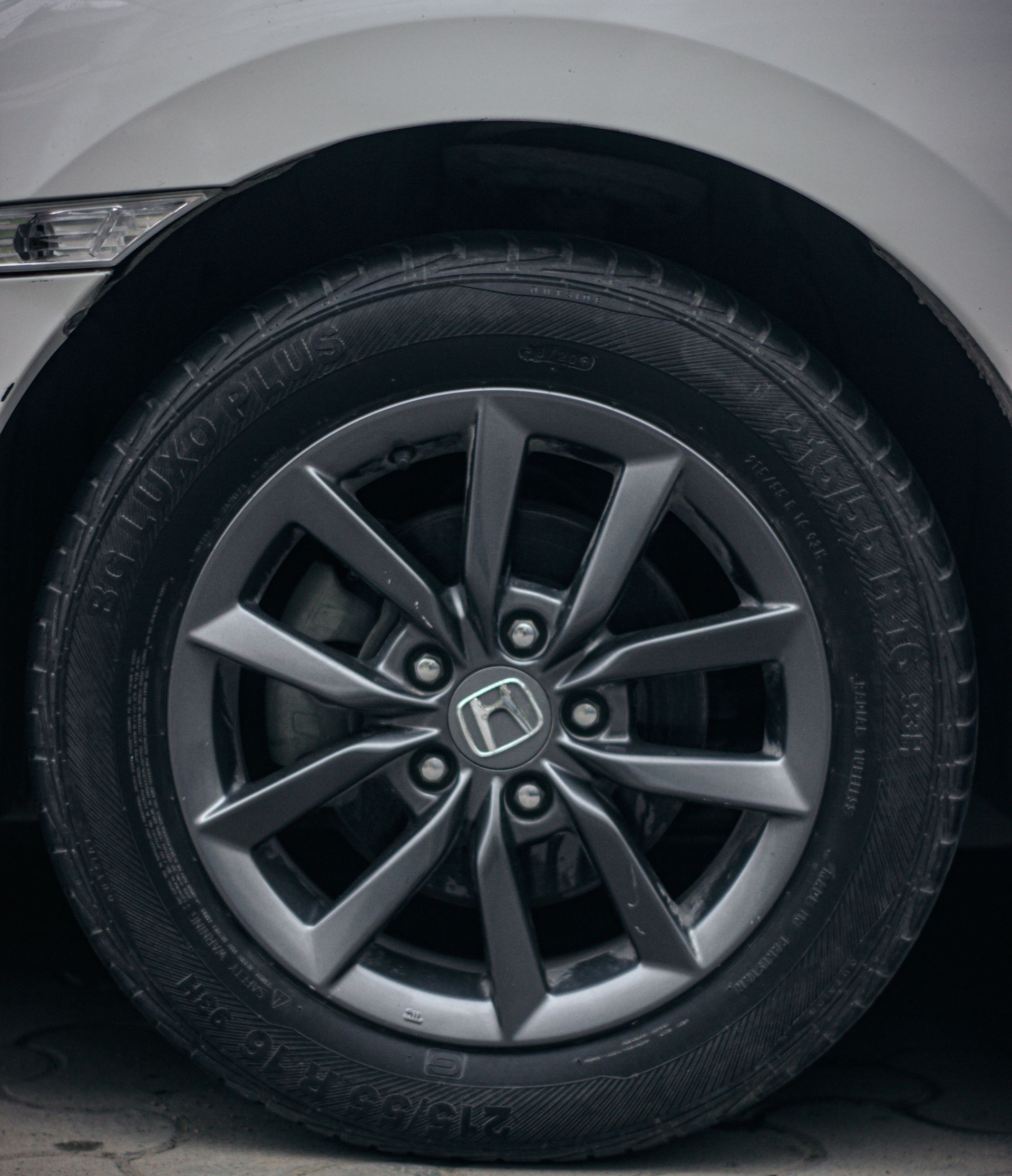 Close-up of a car’s front wheel with a black tire and gray alloy rim on pavement