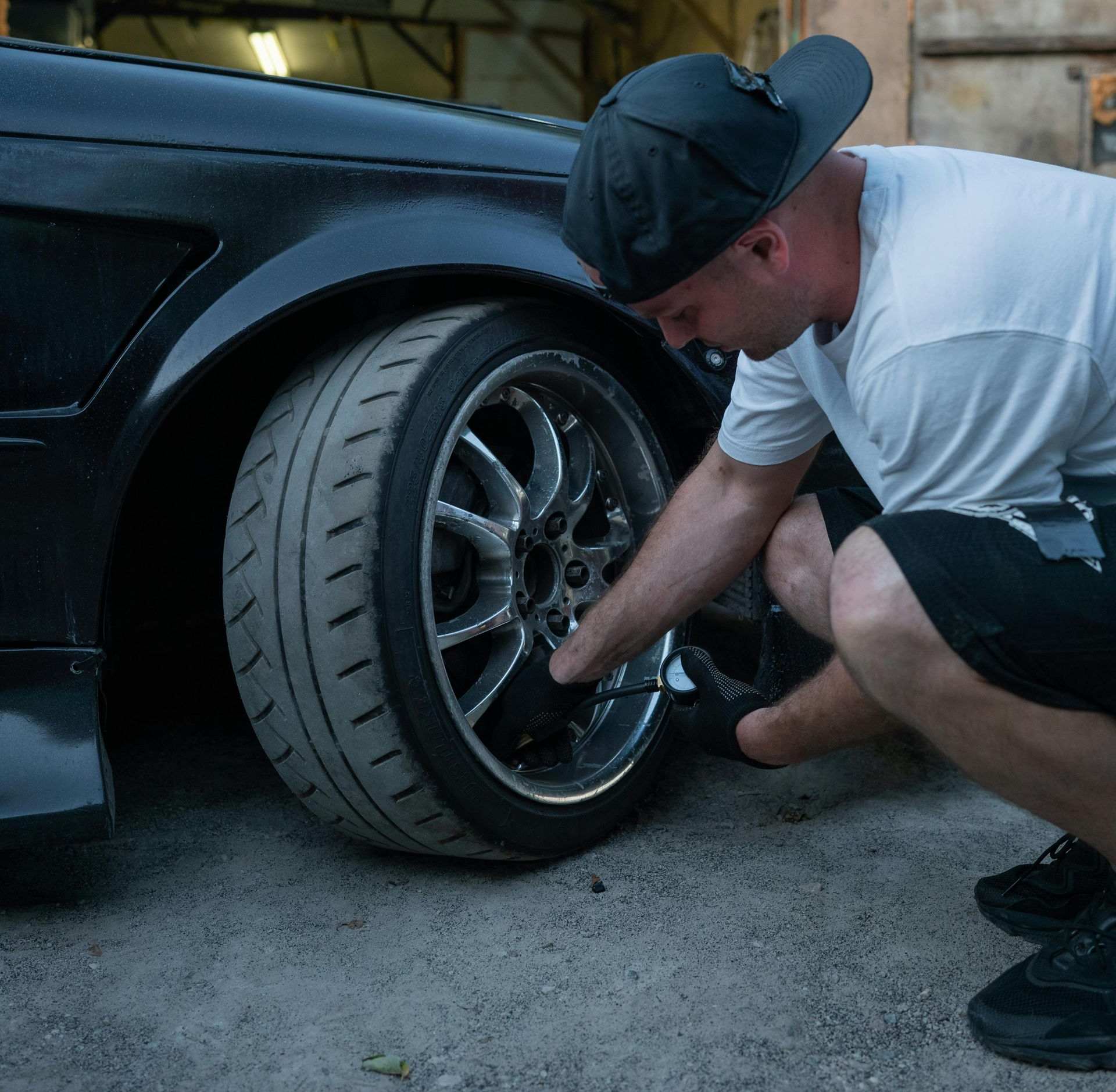 Man kneeling by black car's tire, adjusting it outdoors.