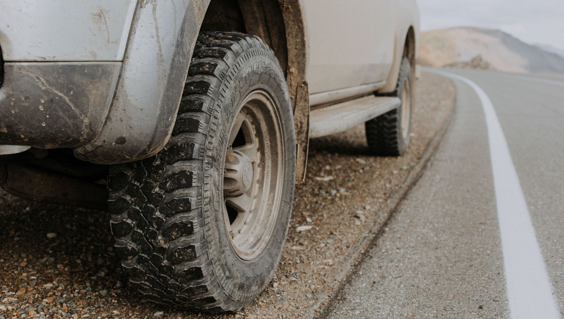 Mud-splattered SUV tire parked on a gravel roadside beside a white lane line