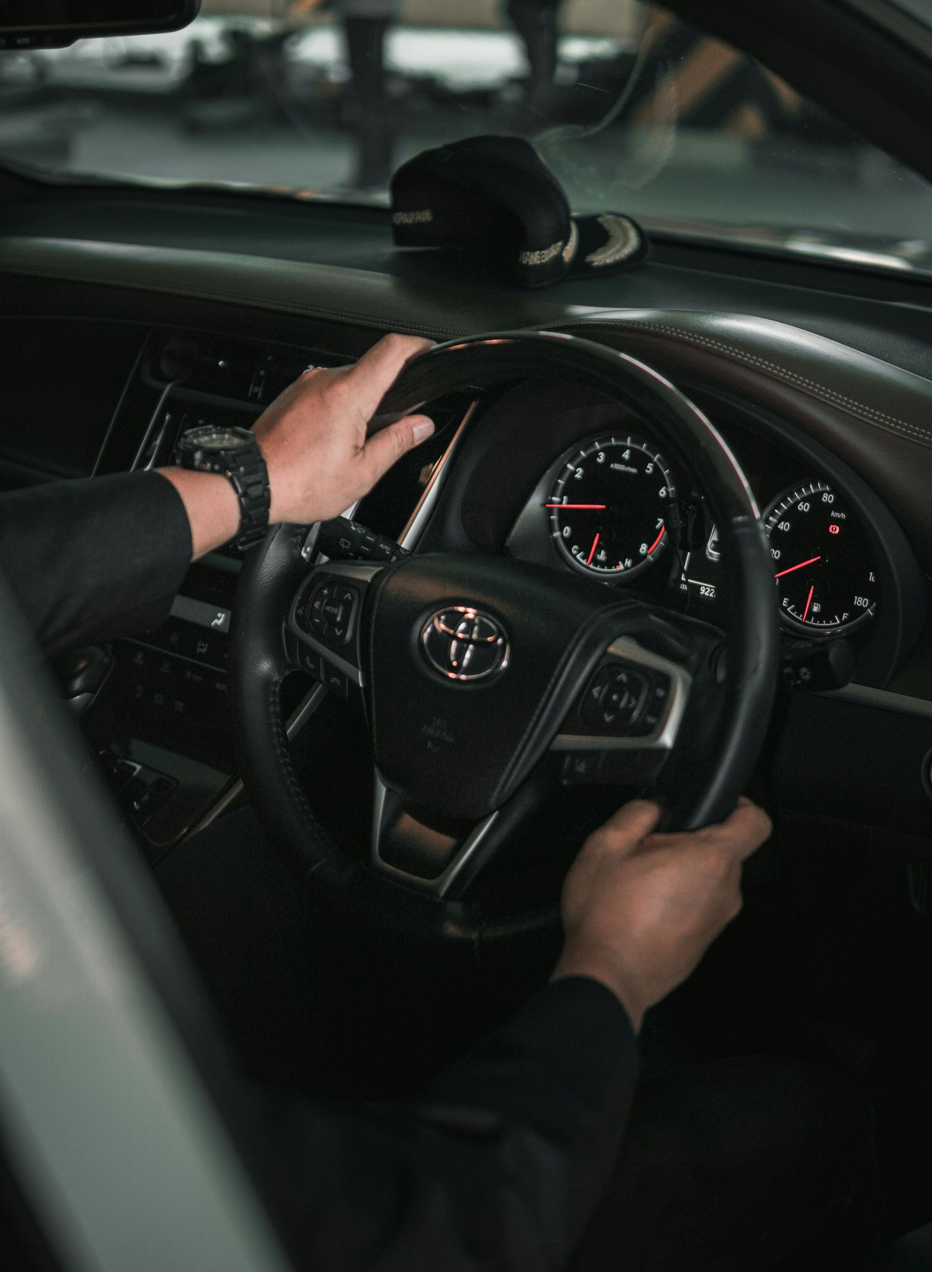 Hands gripping a black steering wheel inside a Toyota car, dashboard visible.