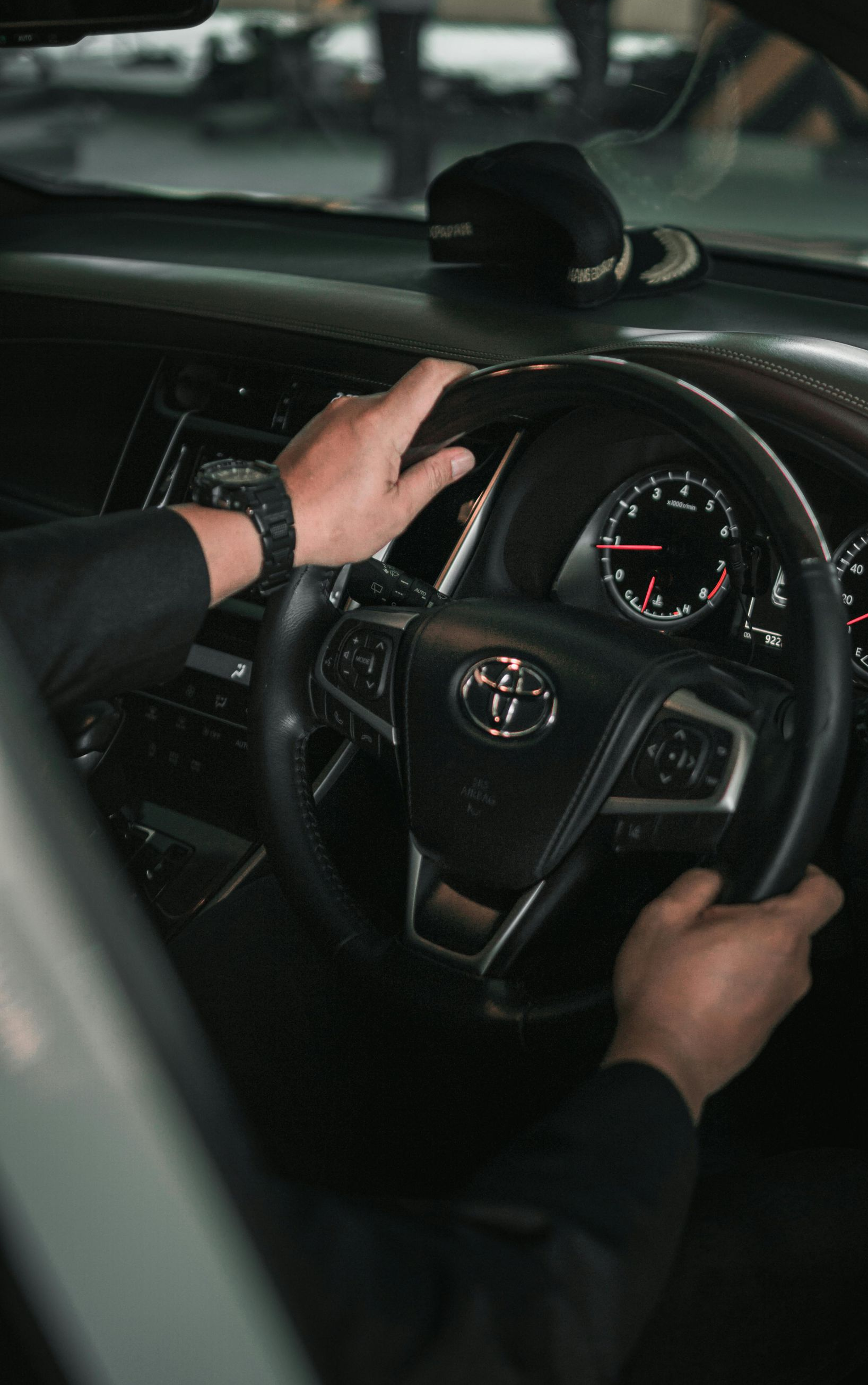 Hands gripping a black steering wheel inside a Toyota car, dashboard visible.