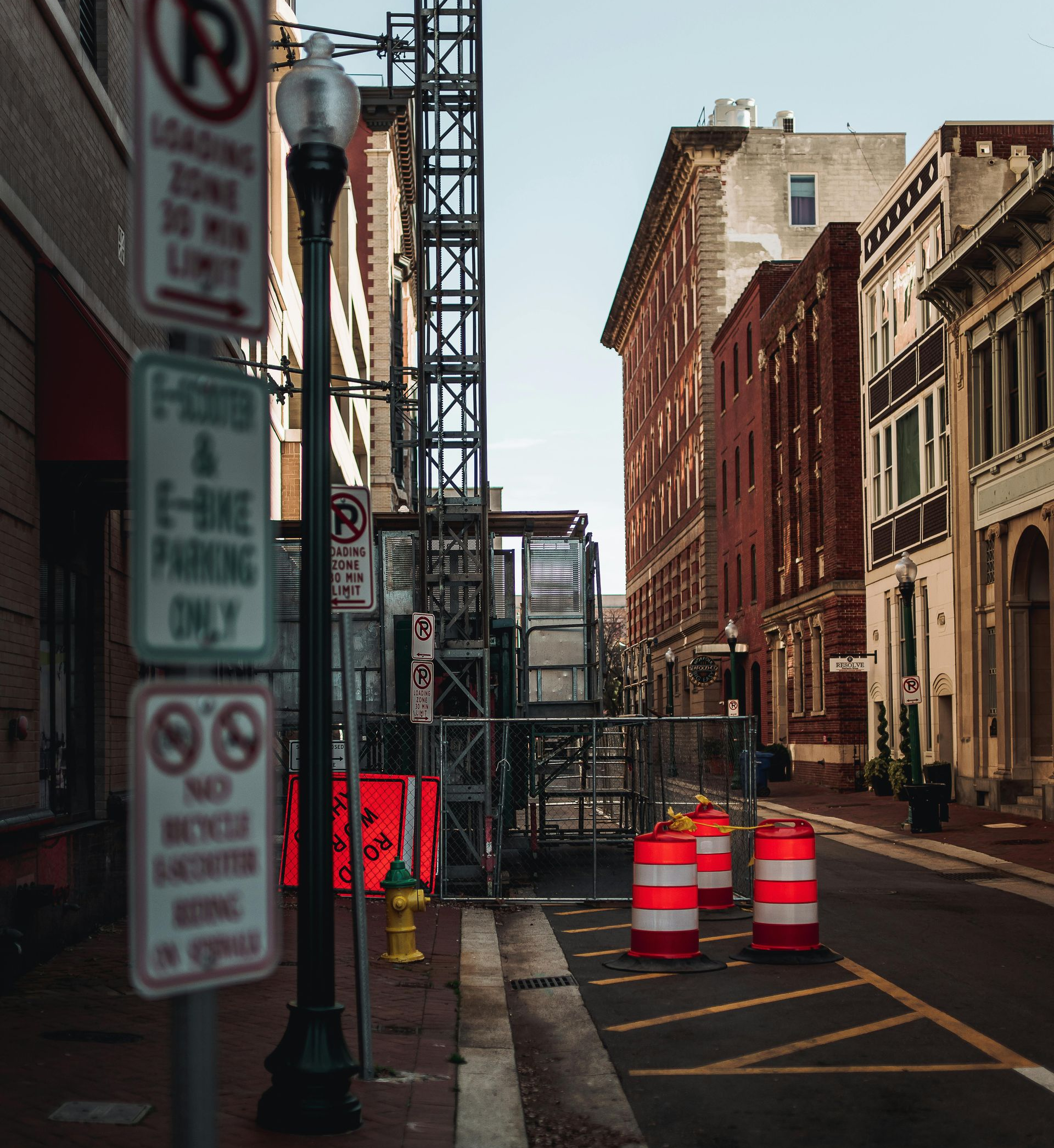 Urban street with construction barrels and signposts beside old brick buildings.