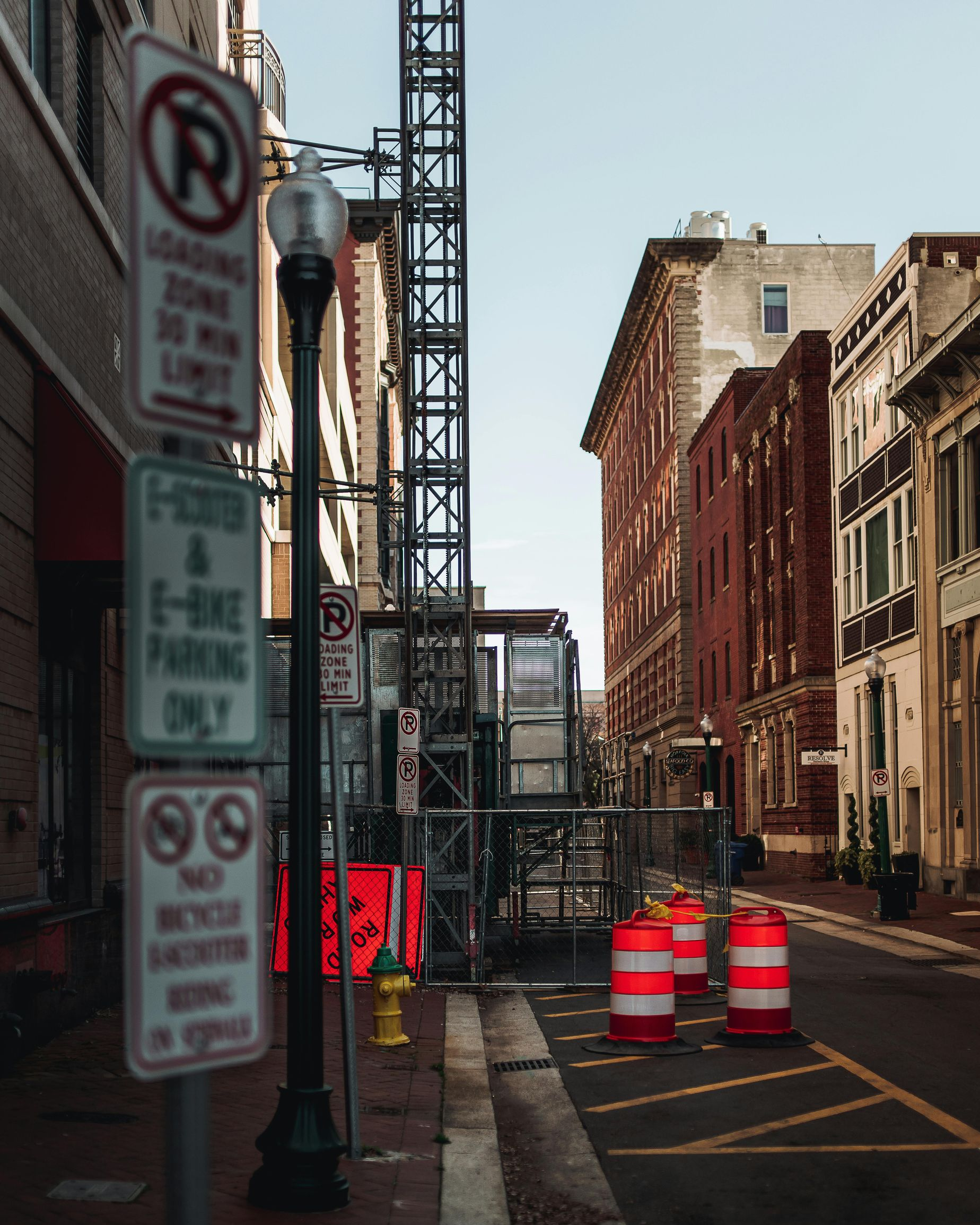 Urban street with construction barrels and signposts beside old brick buildings.