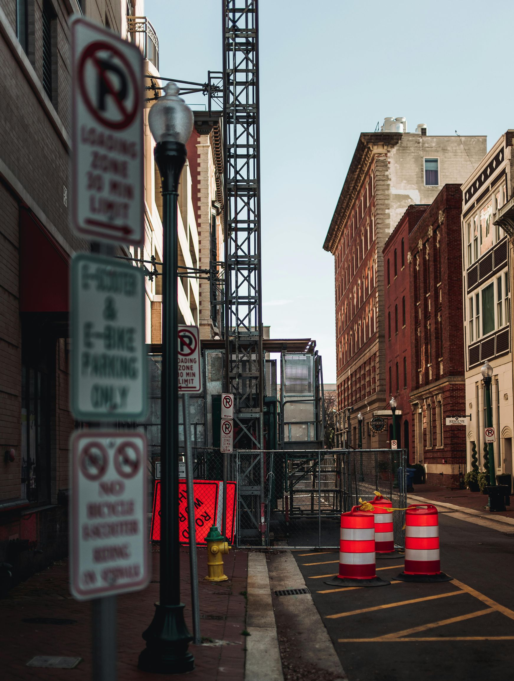Urban street with construction barrels and signposts beside old brick buildings.