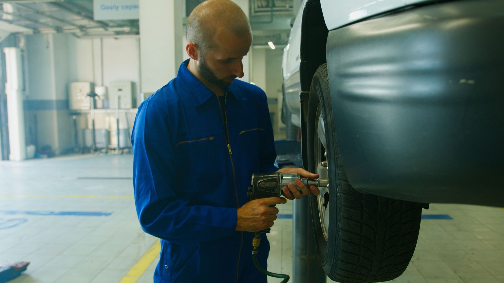 Mechanic in blue coveralls inspecting a car wheel in a garage