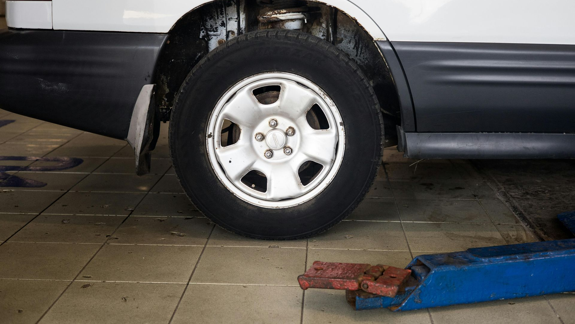 Mechanic in blue jumpsuit using a power tool to work on a car tire in a garage.