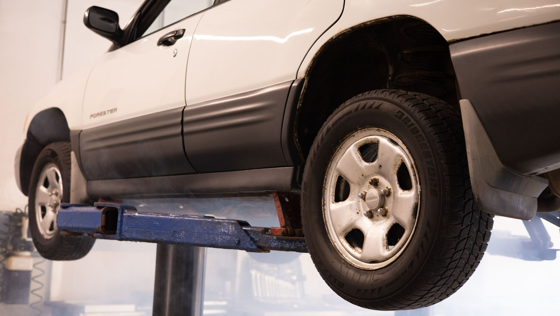 White SUV on a blue hydraulic lift in an auto repair shop