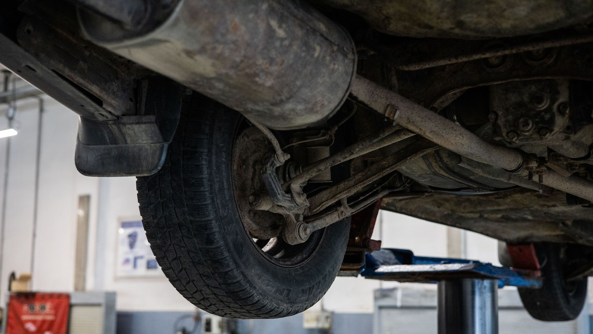 Car lifted on a hydraulic jack in an auto repair shop, with the undercarriage and spare tire visible