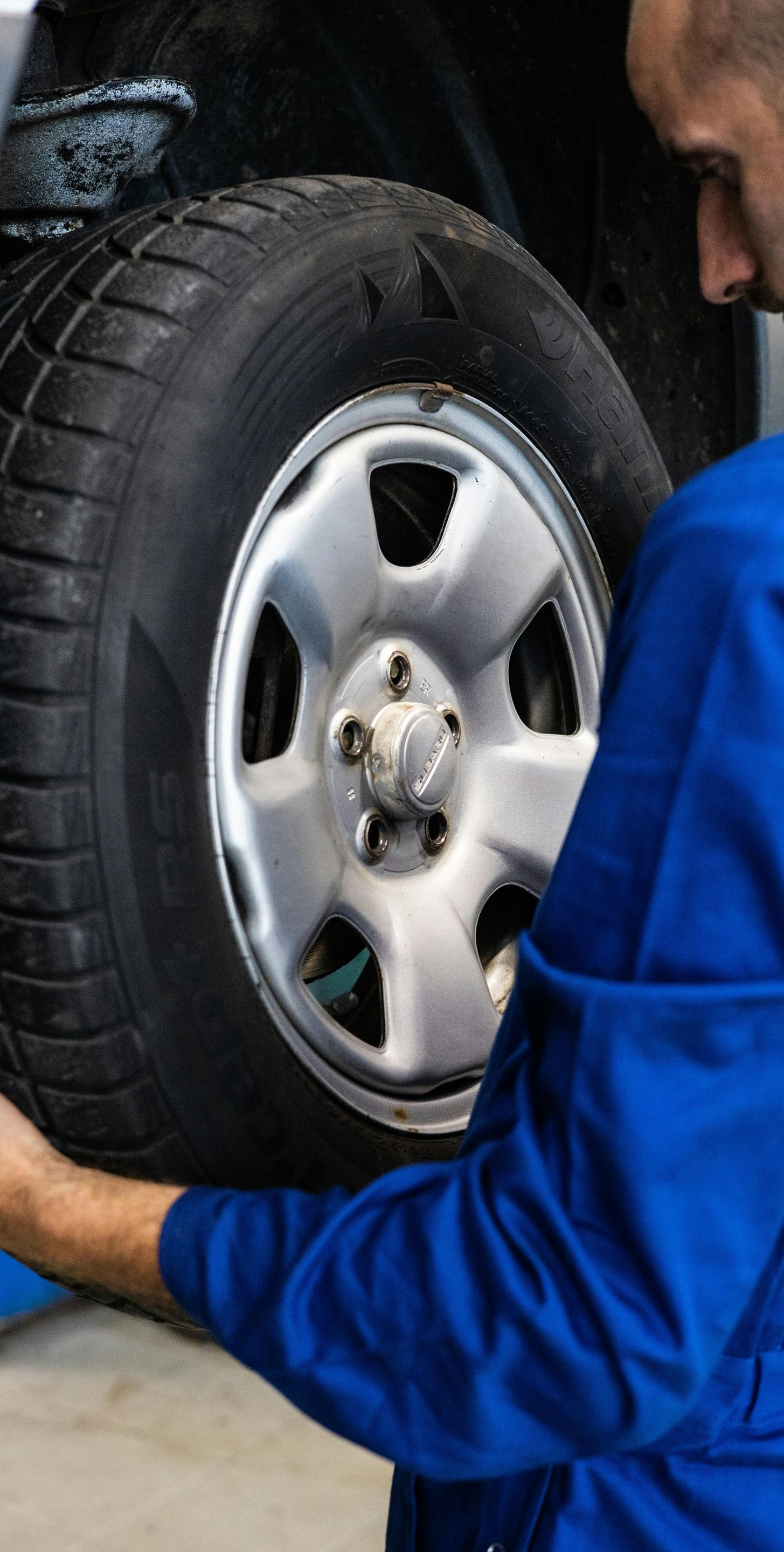 Mechanic in blue coveralls handling a car tire in a garage.