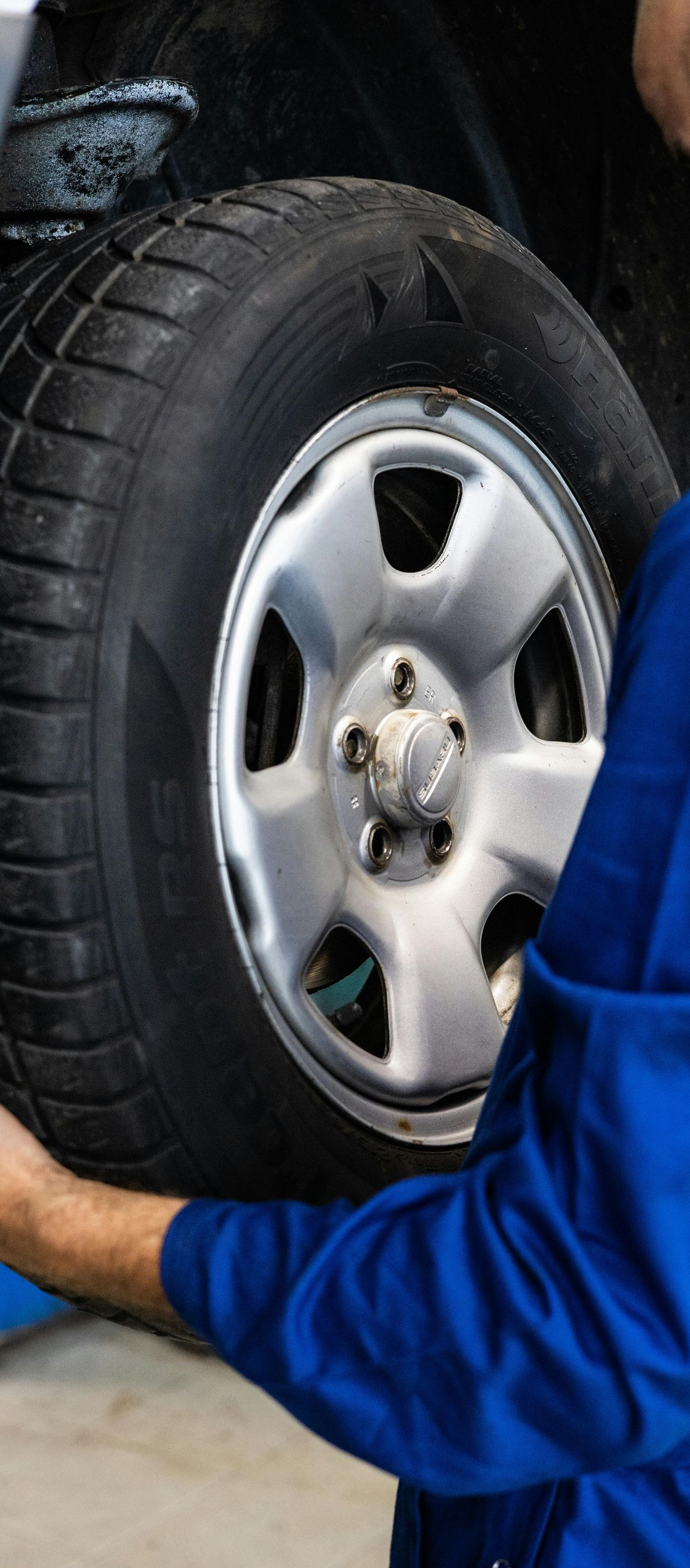 Mechanic in blue coveralls handling a car tire in a garage.