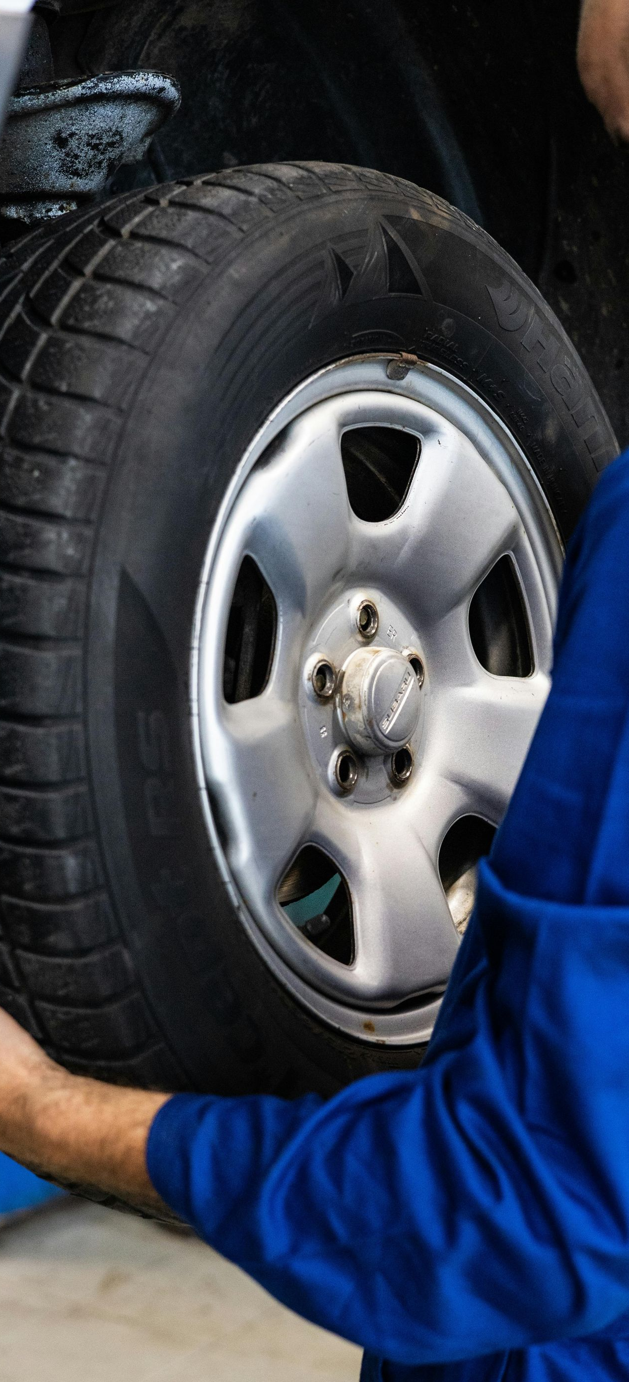 Mechanic in blue coveralls handling a car tire in a garage.