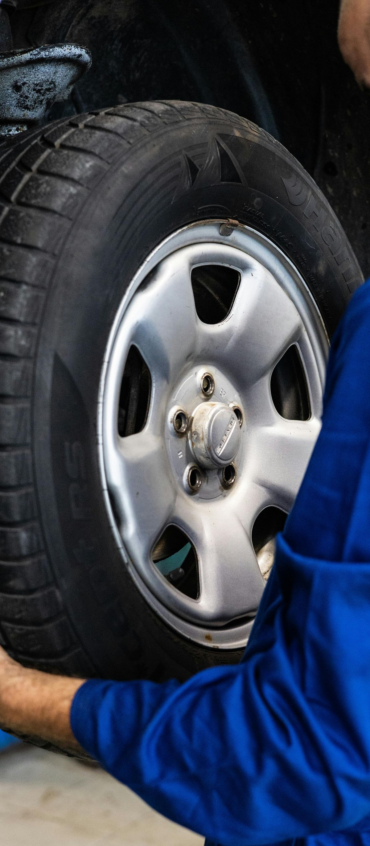 Mechanic in blue coveralls handling a car tire in a garage.