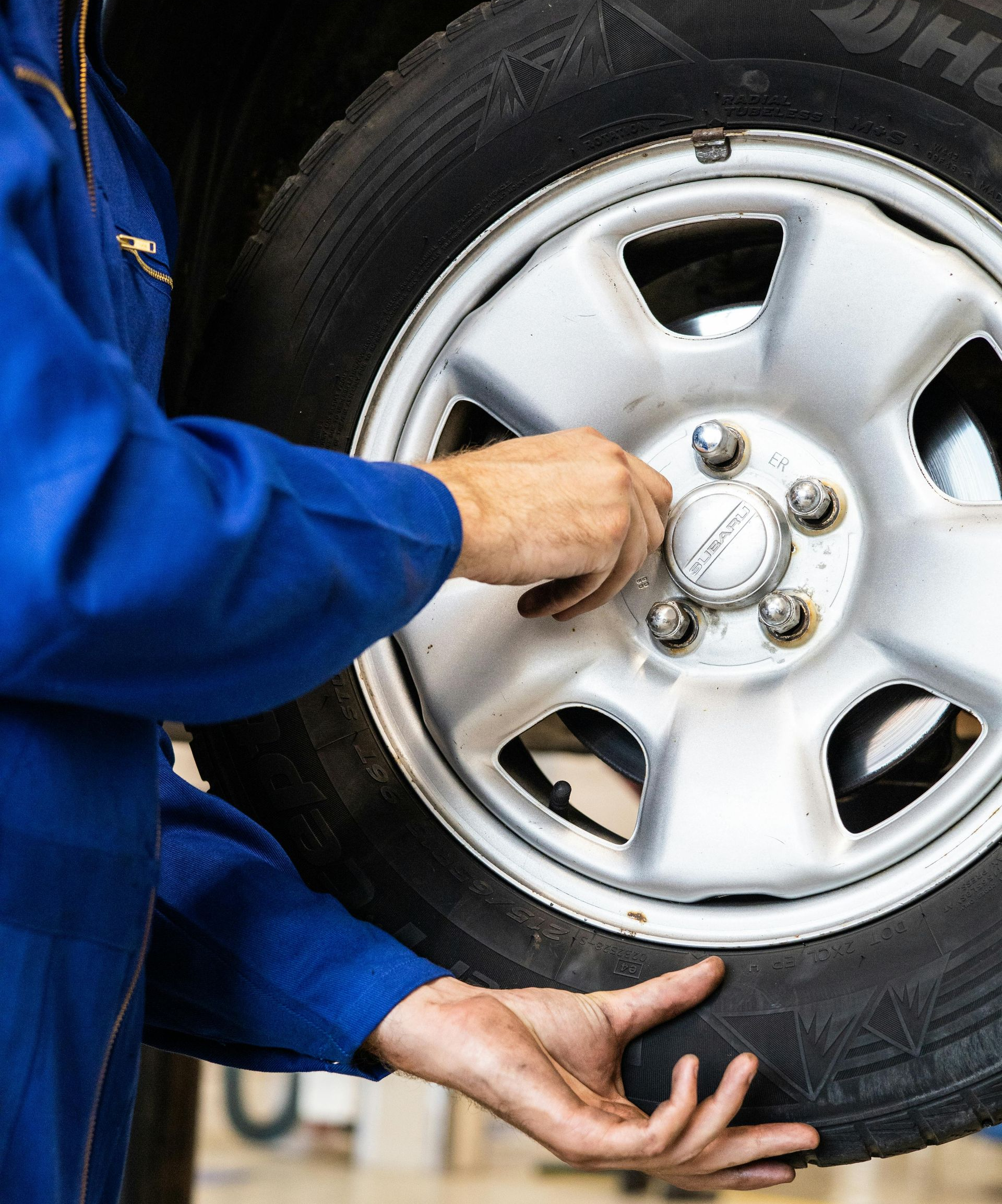 Mechanic in blue coveralls changing a car tire, hands on wheel and hubcap.