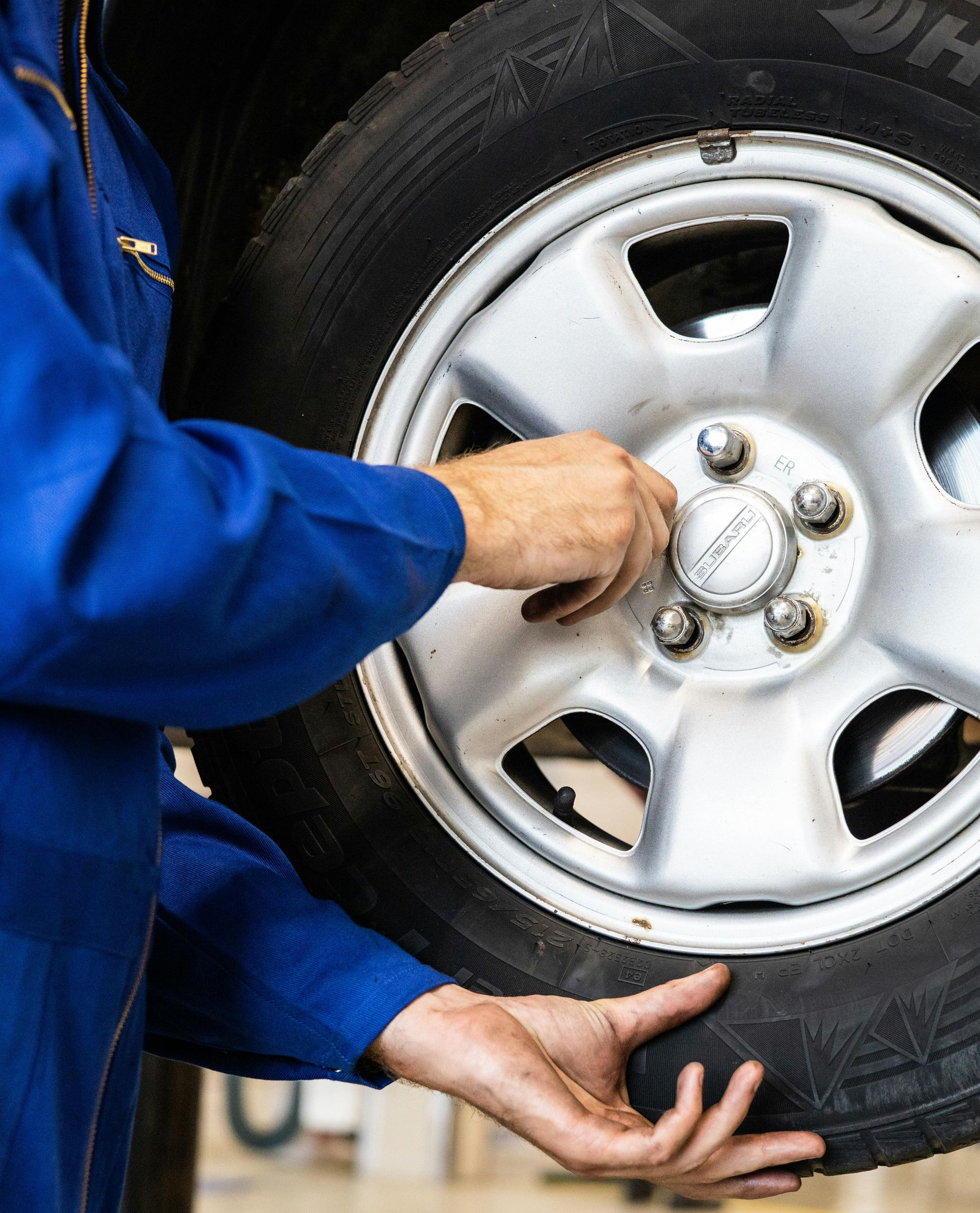 Mechanic in blue coveralls changing a car tire, hands on wheel and hubcap.