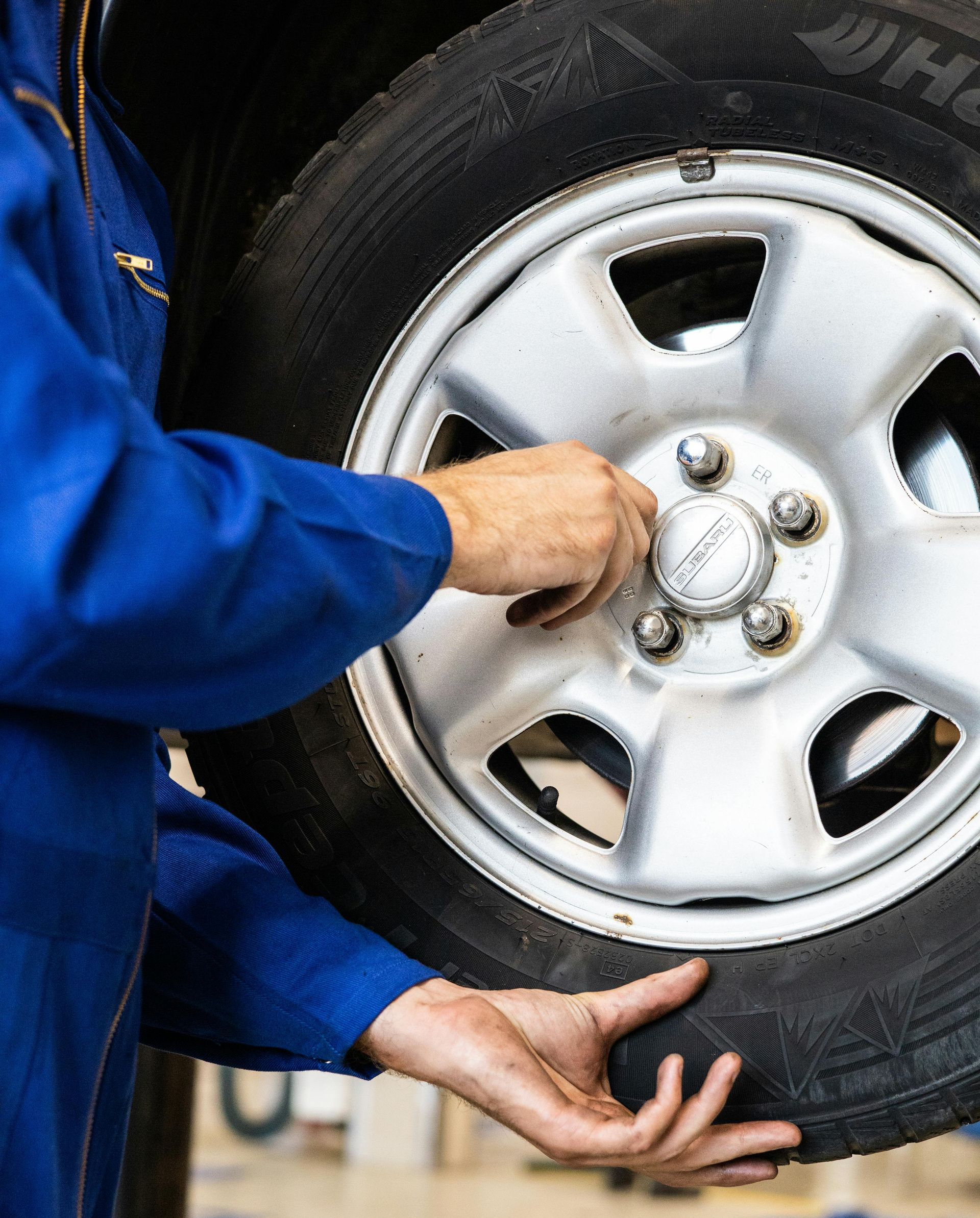 Person in blue jumpsuit working on a car tire, tightening lug nuts.