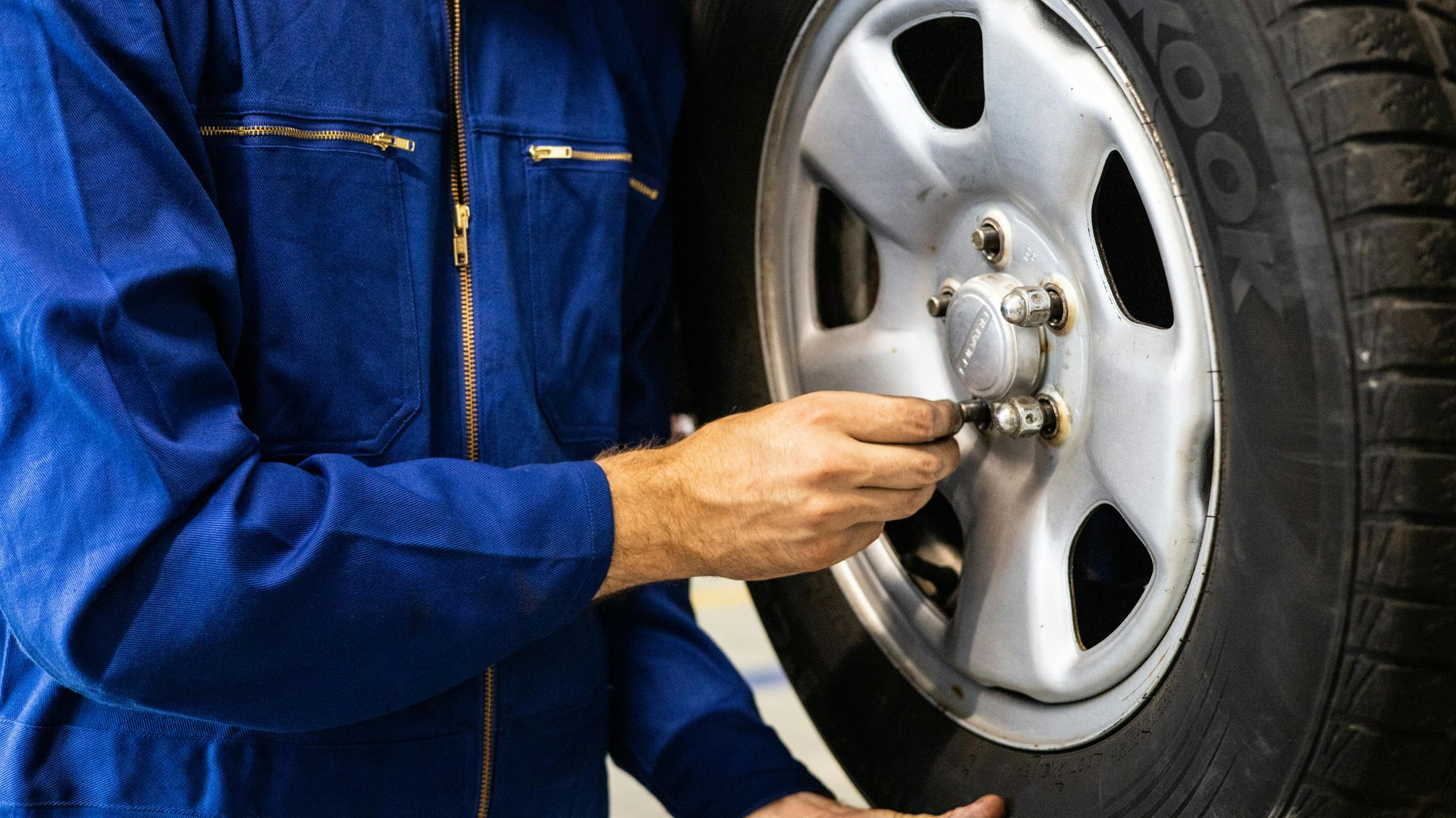 Mechanic in blue coveralls tightening lug nuts on a car tire.