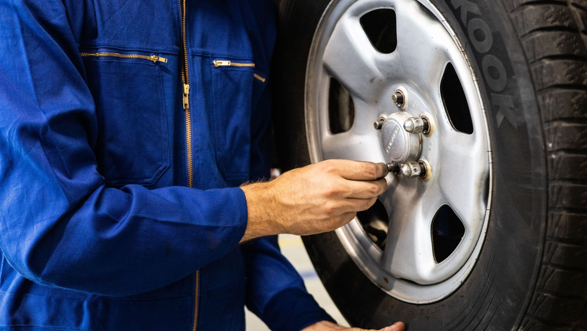 Mechanic in blue coveralls tightening lug nuts on a car wheel with a wrench